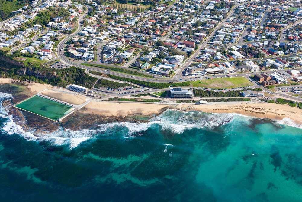 An Aerial View Of A Beach With A Swimming Pool And A City In The Background — Pegar Transport In Newcastle, NSW