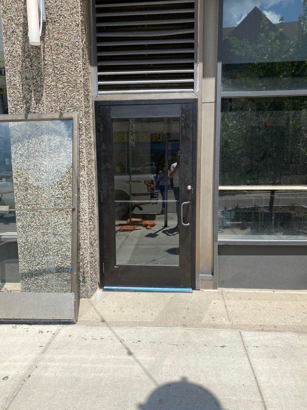 Glass door entrance to a building, reflecting a person. Sidewalk in front.