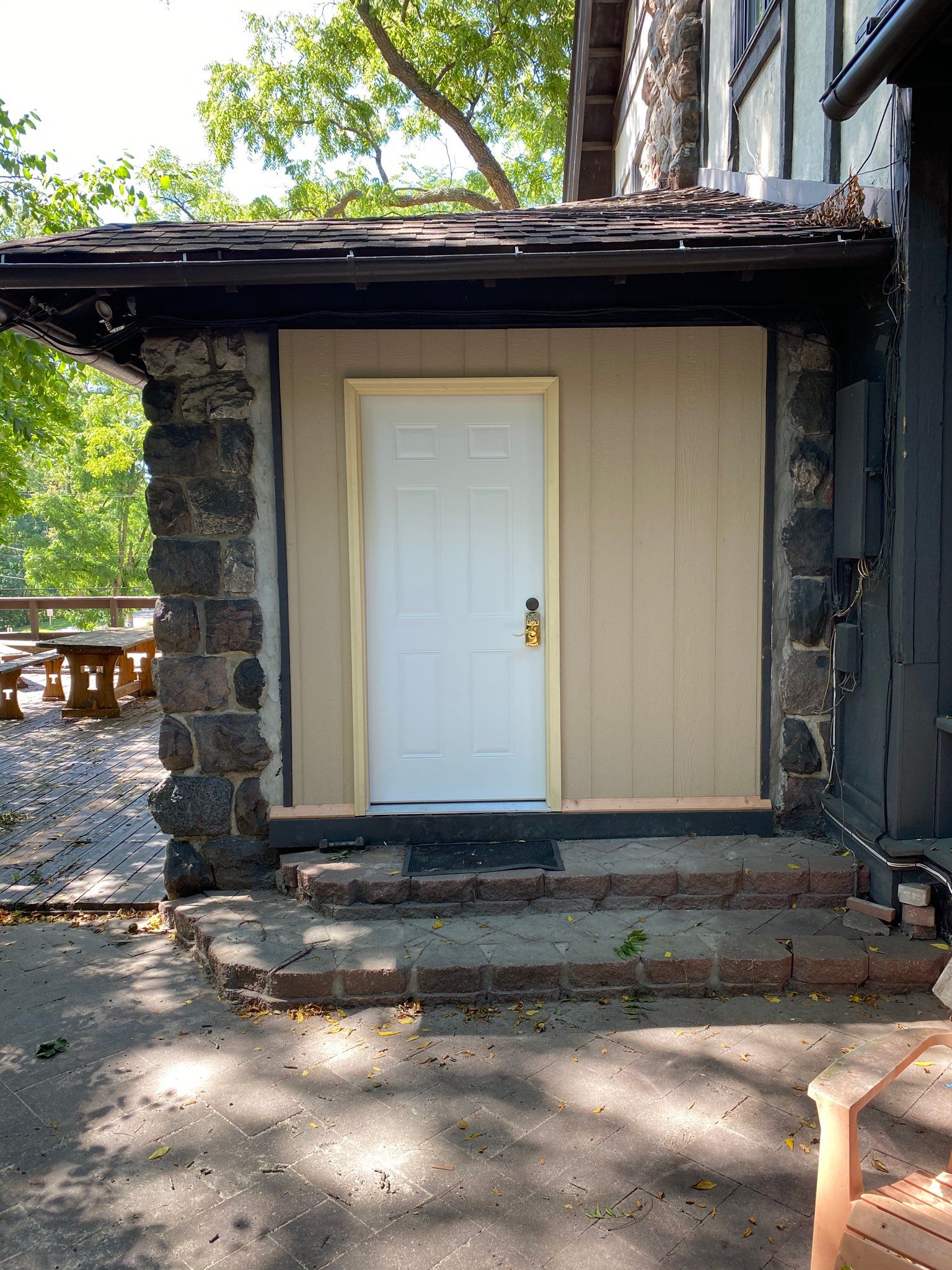 Stone building with a white door, steps, and tan siding.