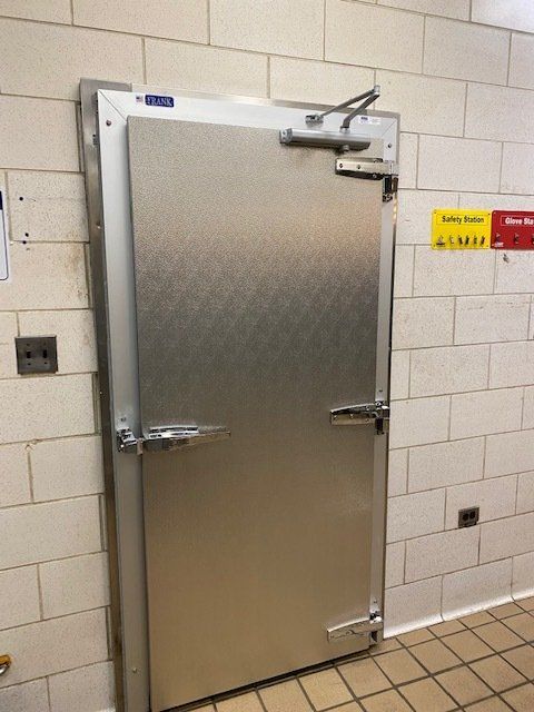 A stainless steel walk-in refrigerator door in a commercial kitchen setting.
