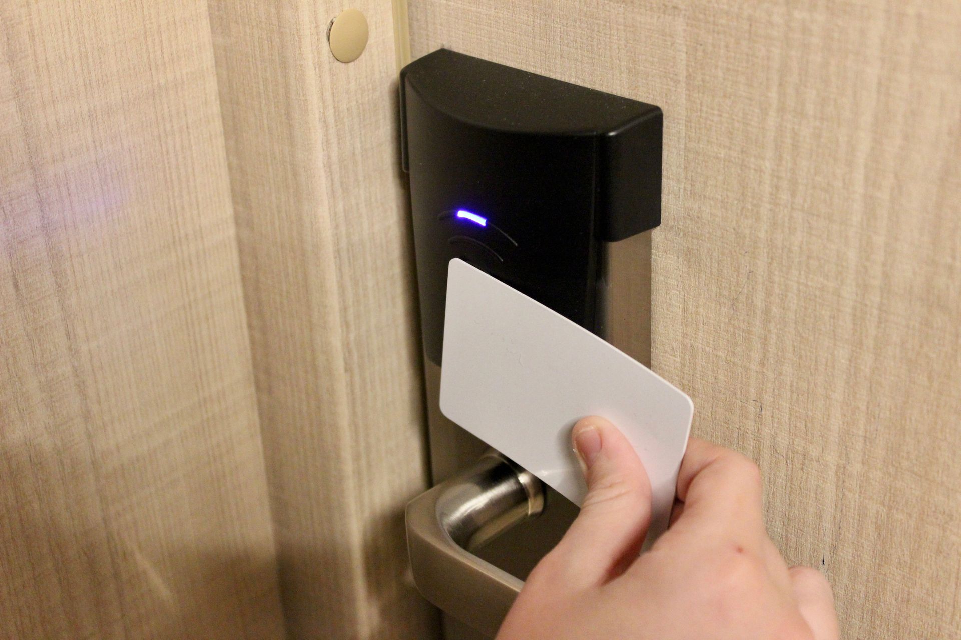 Person using a white key card to unlock a hotel door. The door lock is black and silver.