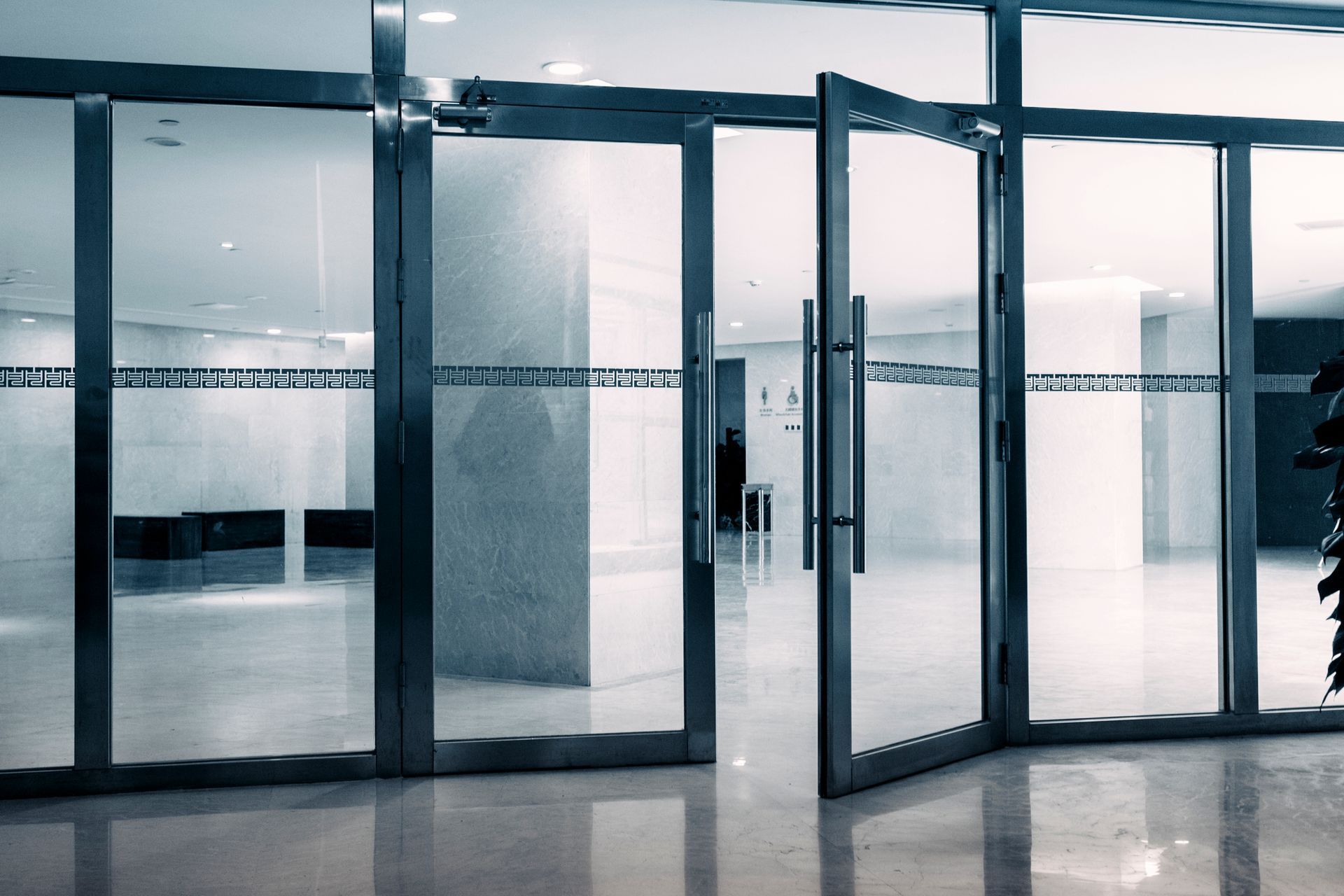 Modern glass commercial doors open to a bright lobby with marble floors and clean design.