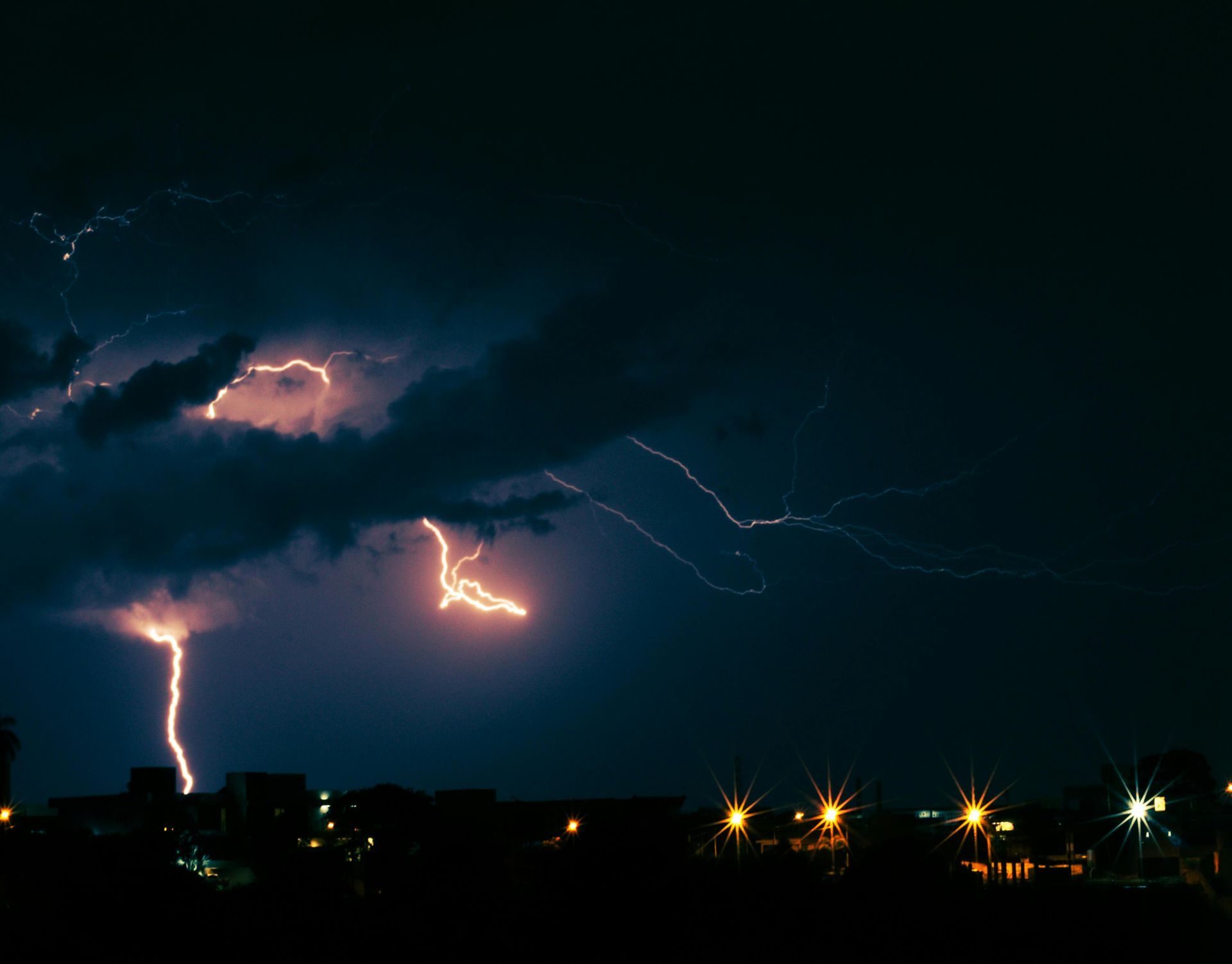 Lightning striking over a dark night skyline with glowing city lights below