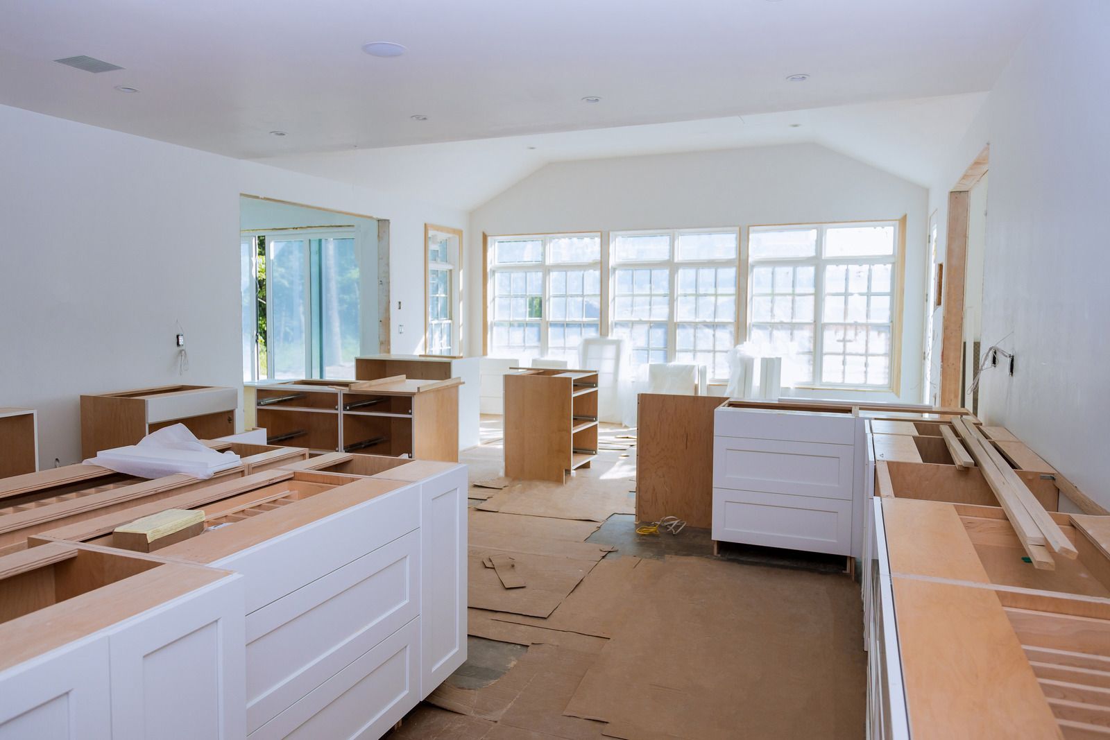 Kitchen renovation in progress: cabinetry installed, windows covered, construction materials present.