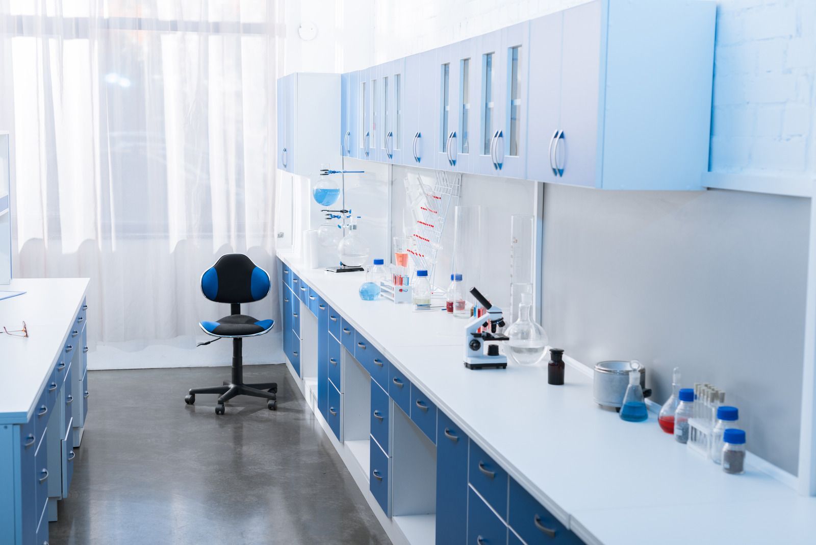 Laboratory with blue and white cabinets, equipment on a long counter, and a lab chair.
