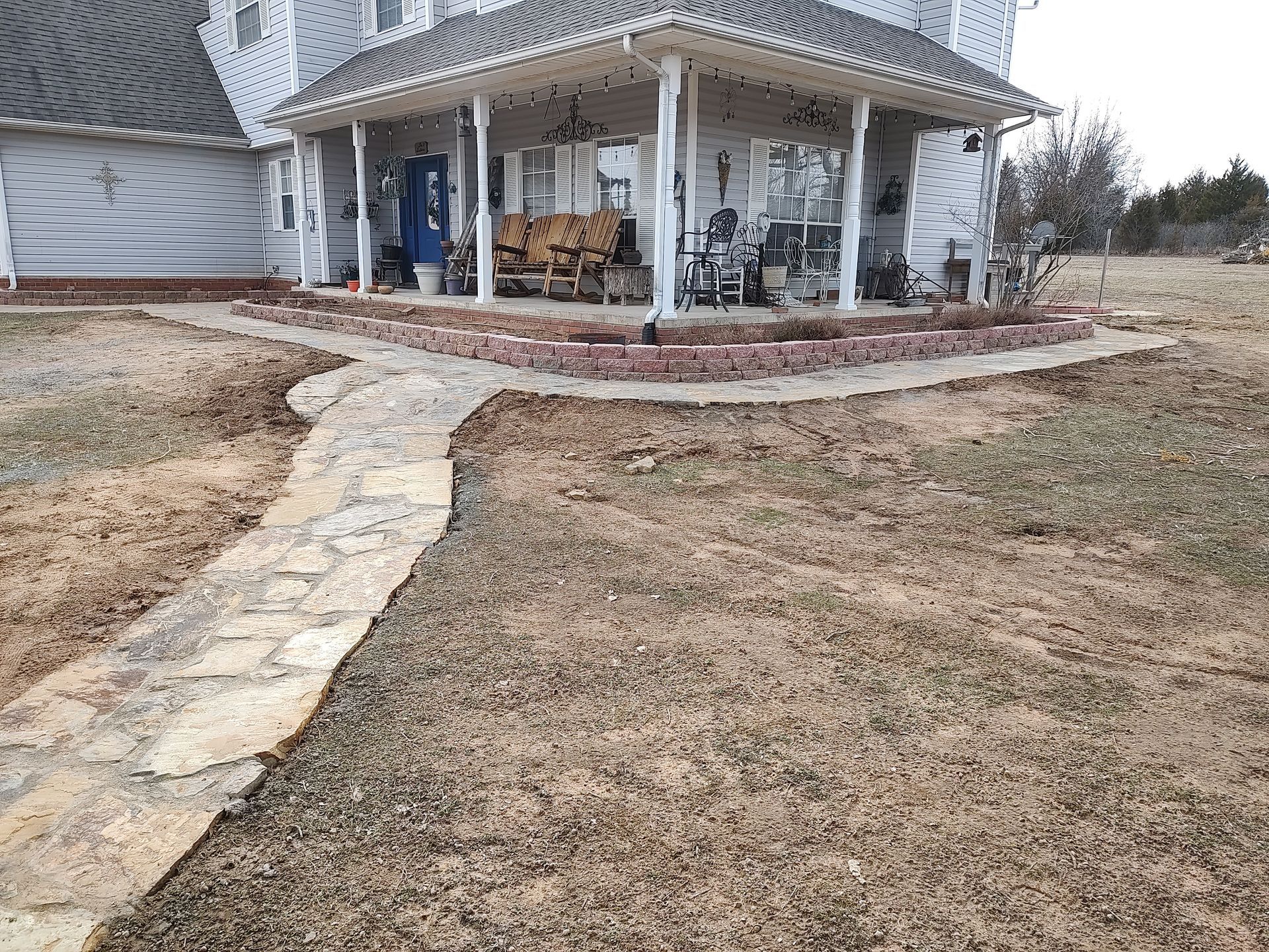 Stone walkway leading to a house with a porch. Brown grass surrounds the path and building.
