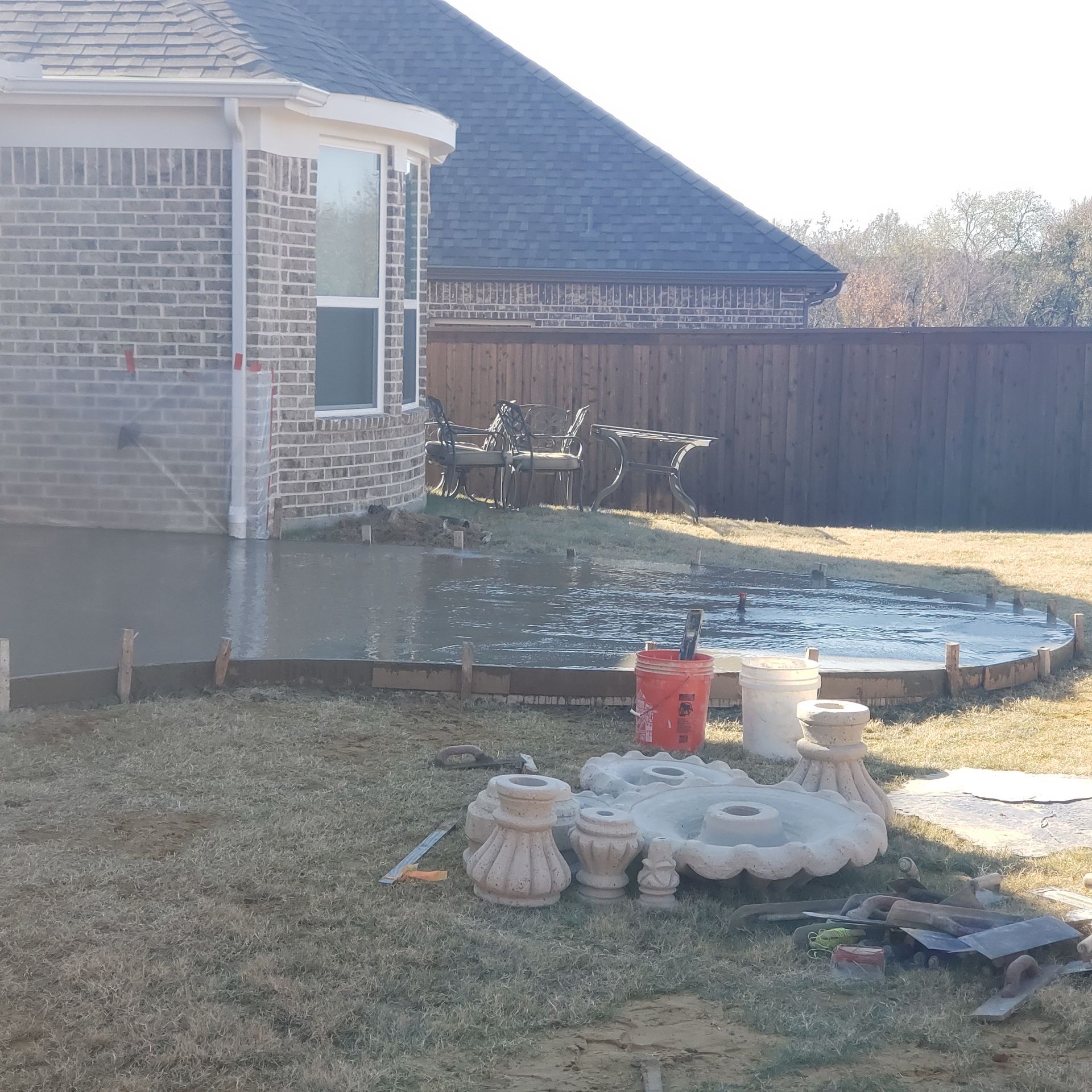 Concrete patio being poured near a brick house. Fountain parts sit nearby.