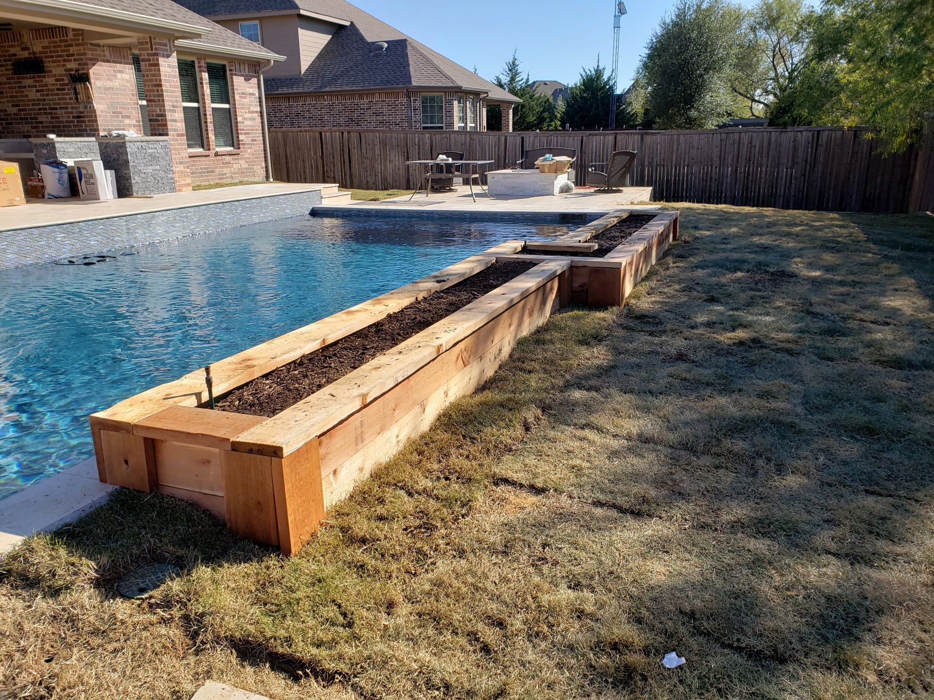 Wooden planter box next to a pool filled with soil, grass lawn.