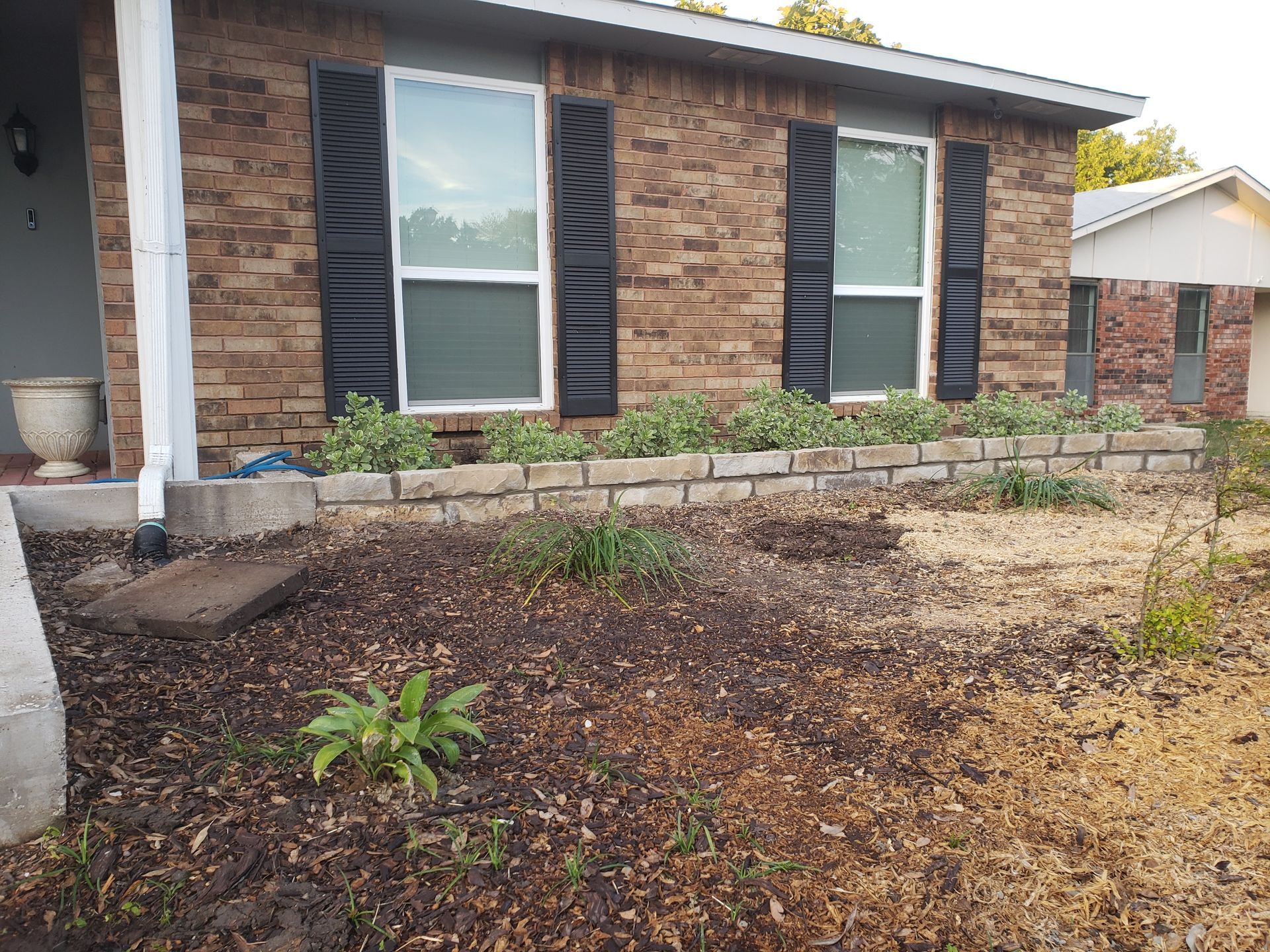 Brick house with black shutters, flower bed, and mulch.
