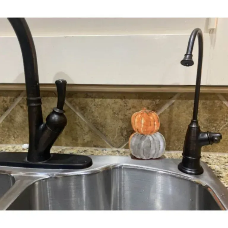 Kitchen sink with black faucet and two small stacked decorative pumpkins by the backsplash