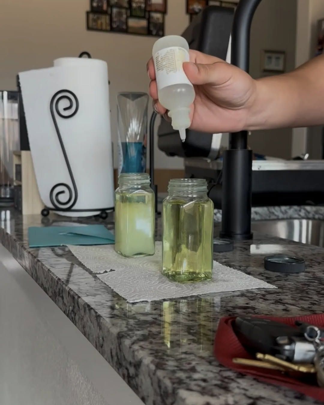 Hand pouring clear liquid into a glass jar on a kitchen counter with two other jars nearby