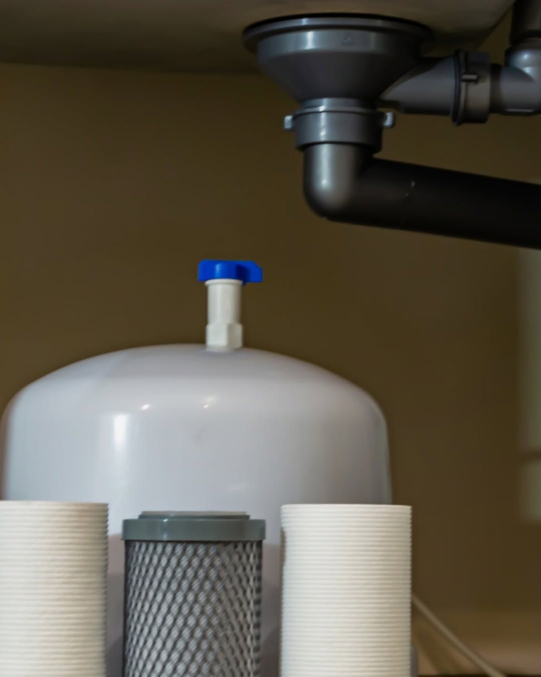 Under-sink water filtration tank with blue valve and black plumbing pipes above it
