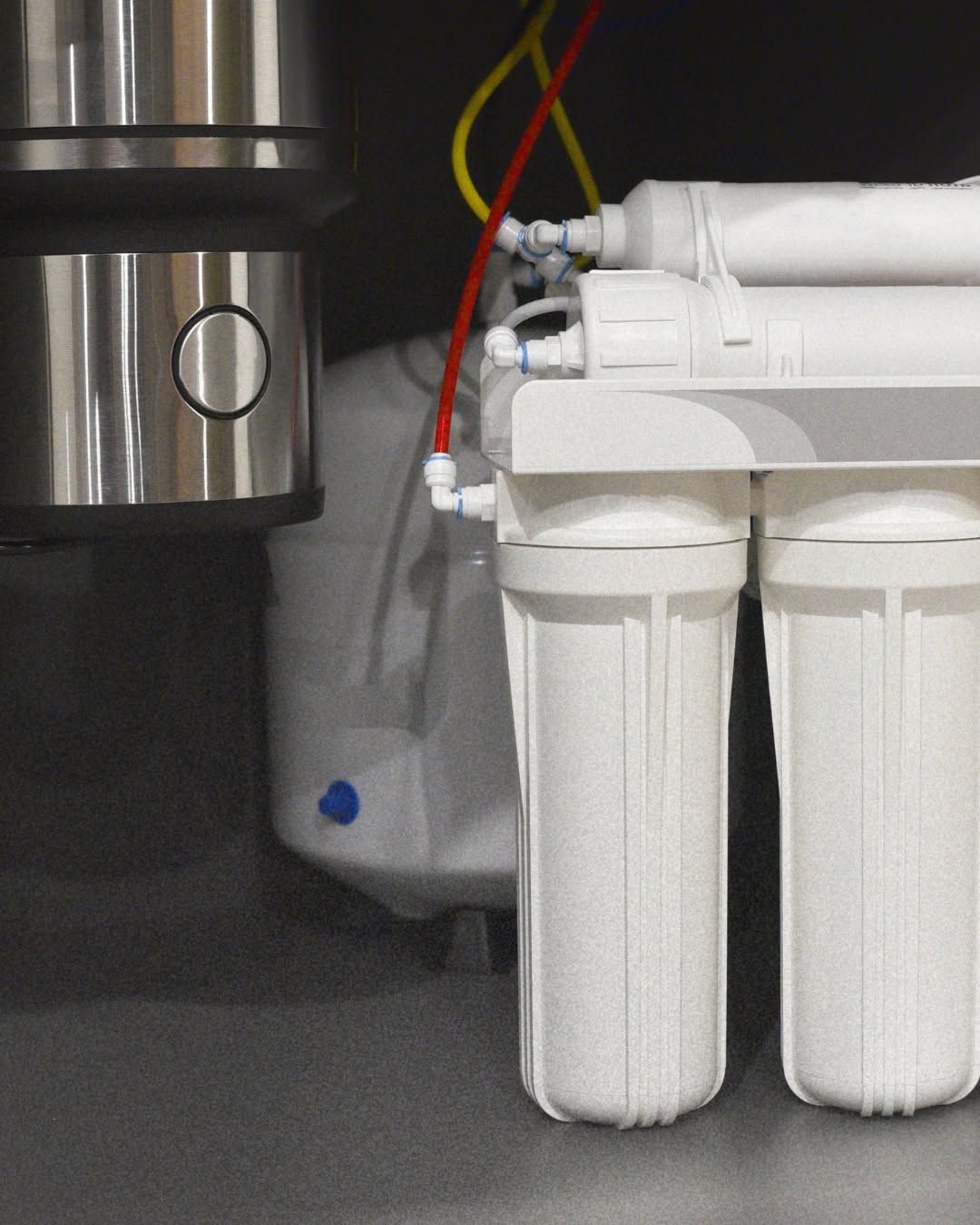 Under-sink water filtration system with white filter cartridges and connected red, yellow, and black tubes