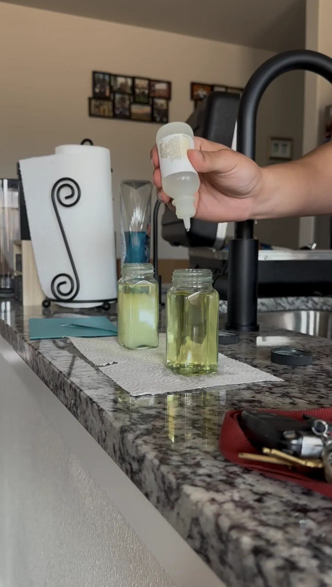 Hand holding a white bottle over three small green glass bottles on a kitchen counter.