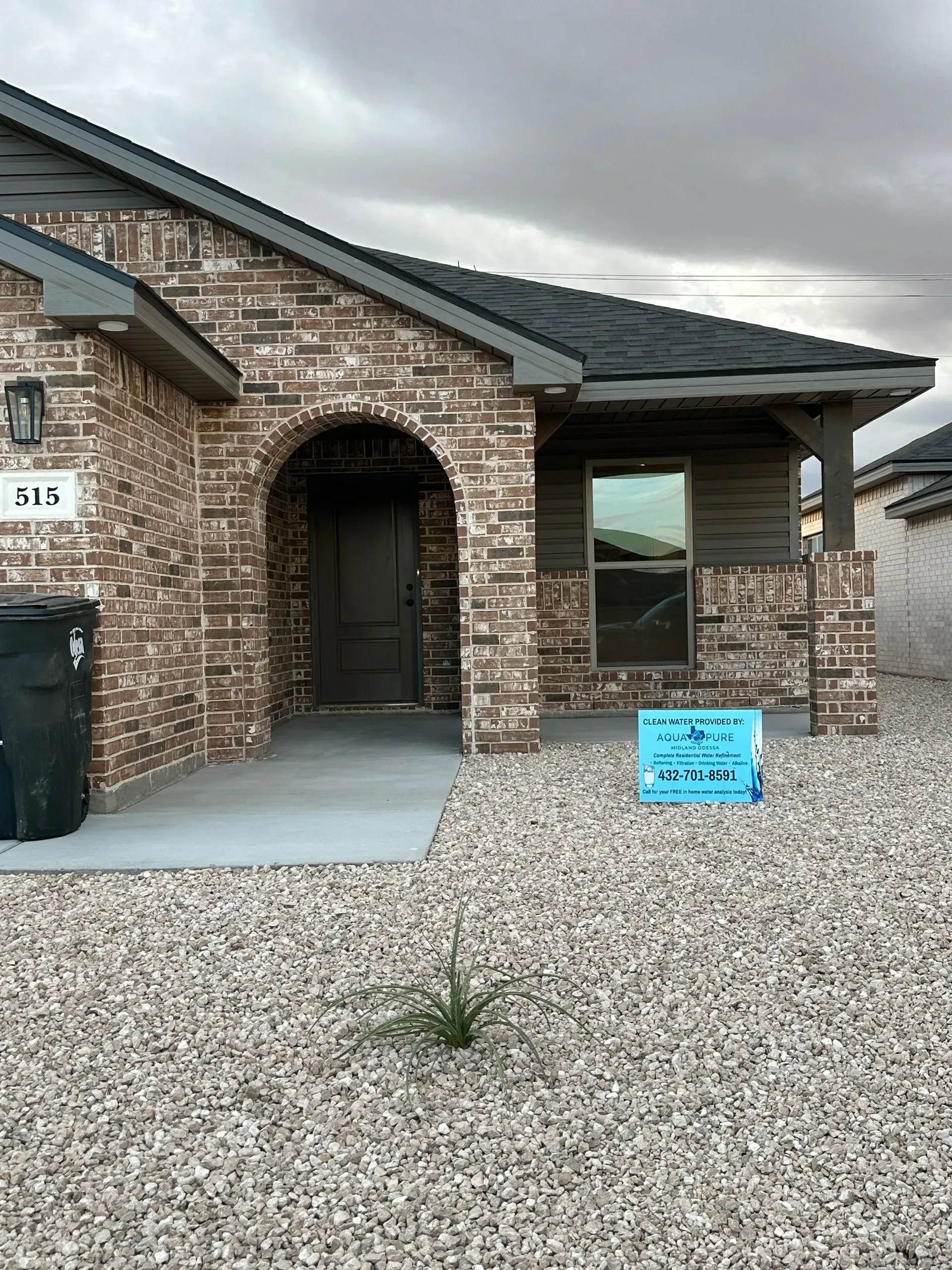 Brick house with arched entry, gravel yard, and cloudy sky.
