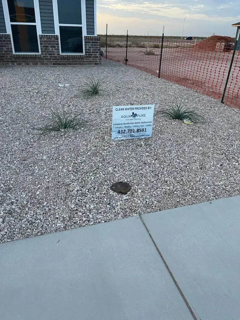 Gravel yard beside a house with a small sign and orange construction fencing beyond.