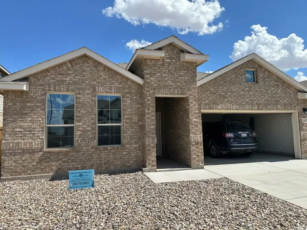 Brick single-story house with a two-car garage and gravel front yard under a blue sky.