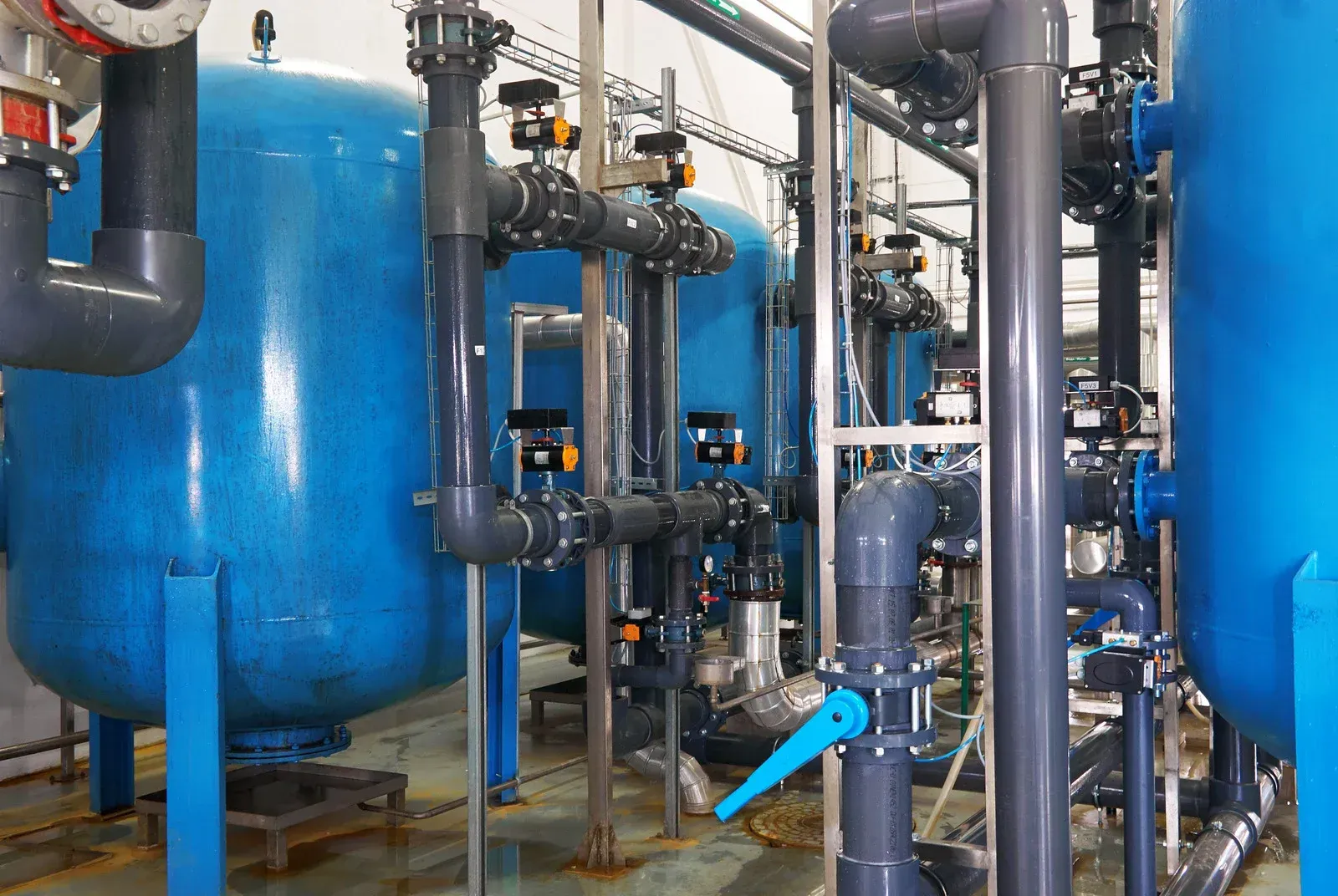 Blue industrial tanks and pipes in a mechanical room, with valves and gauges.
