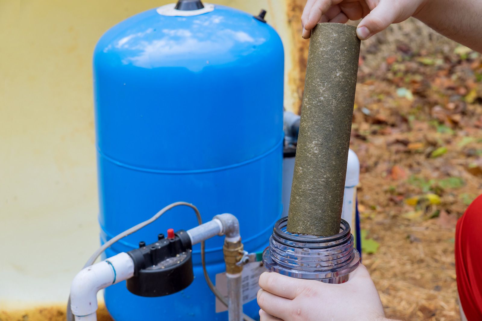 Hands installing a cylindrical filter into a blue water treatment tank outdoors