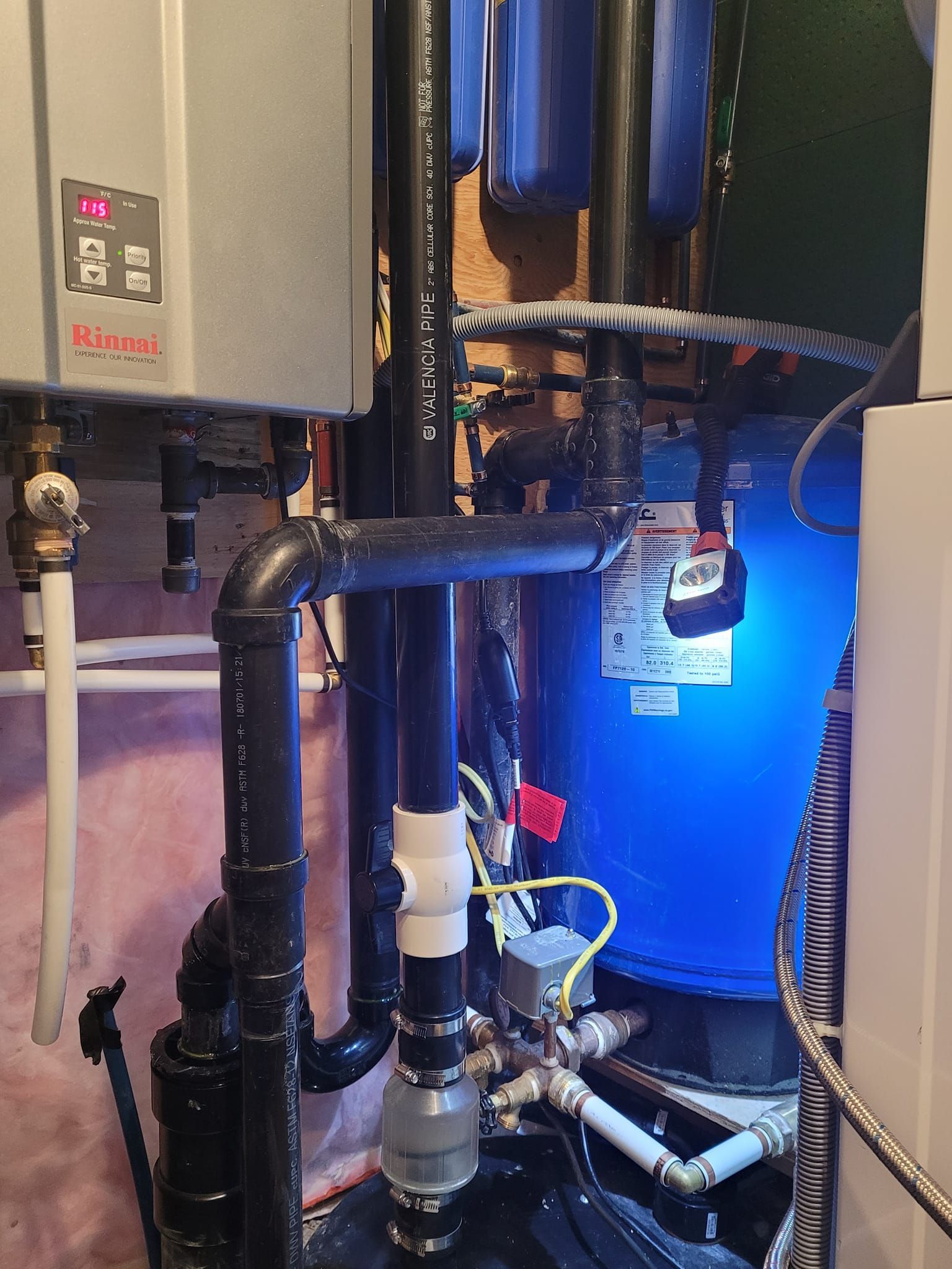 Plumbing system with water heater, filters, and pipes in a basement setting. Blue glow illuminates the filter tank.