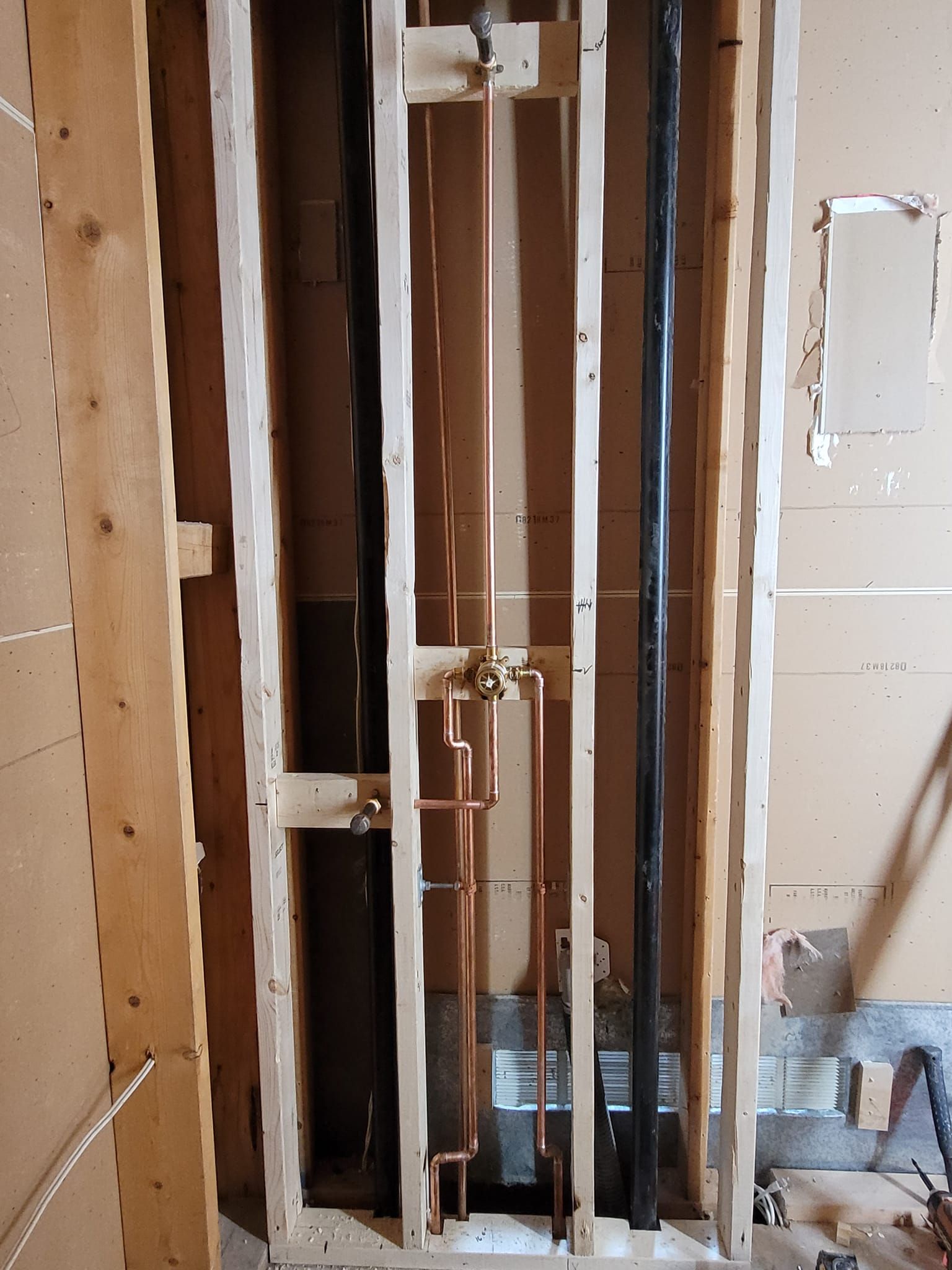 Framed wall showing new copper and black pipes, and faucet valves installed.