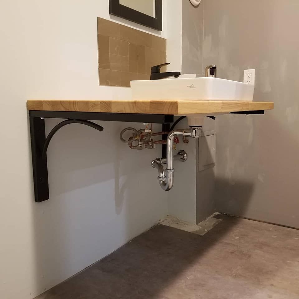 Floating wooden bathroom sink with black hardware, mounted on black metal brackets, set against a white and gray wall.