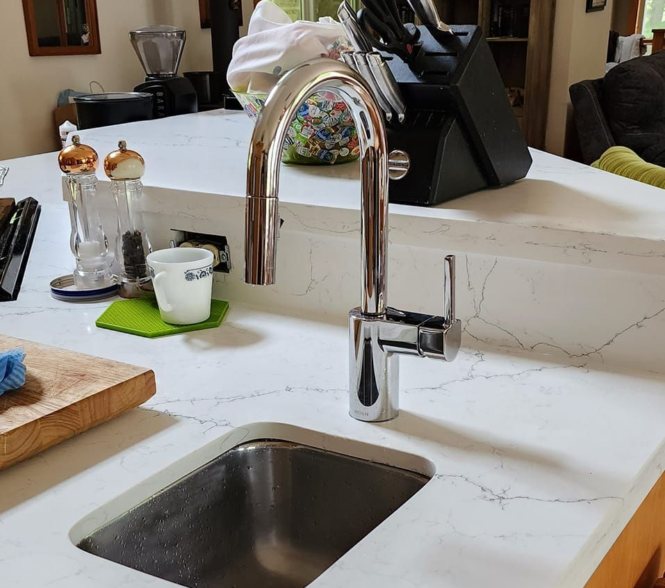 A person uses a wrench to tighten a chrome pipe under a sink.