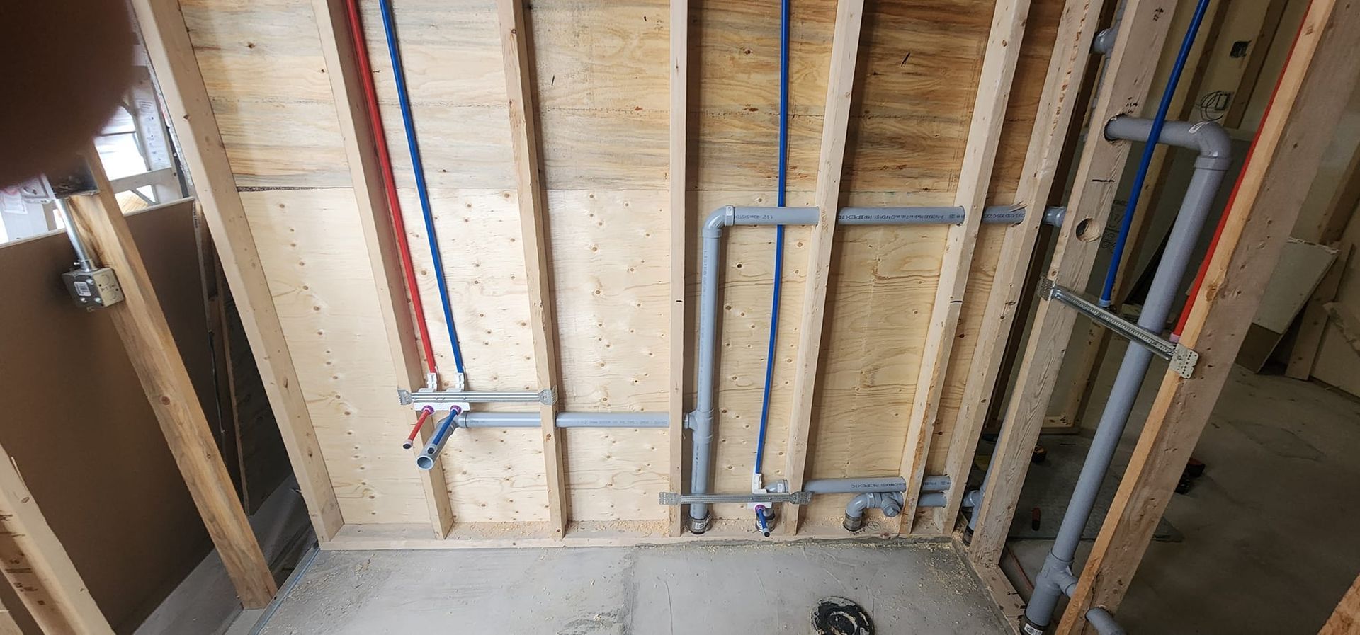 Bathroom construction: plumbing pipes installed on wooden wall. Red and blue pipes. Gray drain pipes.