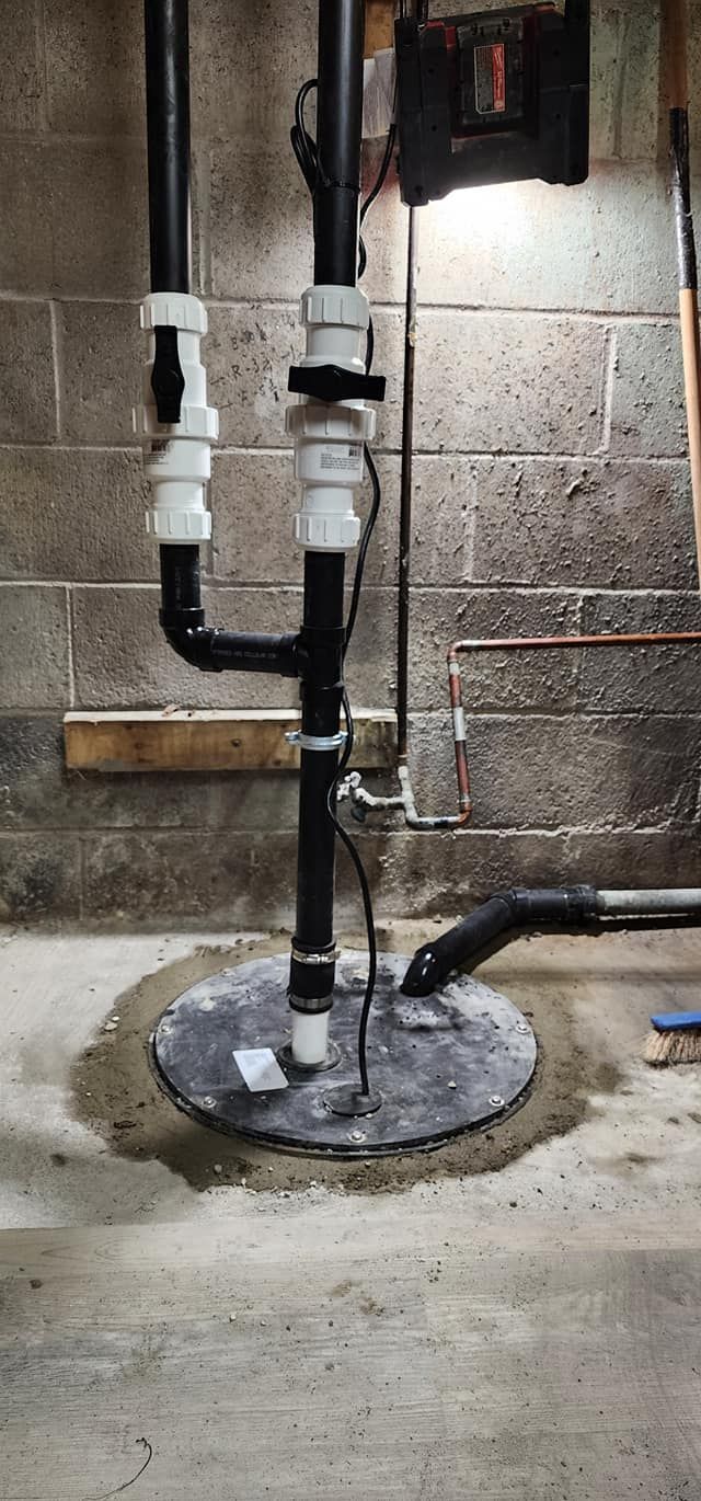 Sump pump installation in a basement with black and white piping and a grey circular lid.