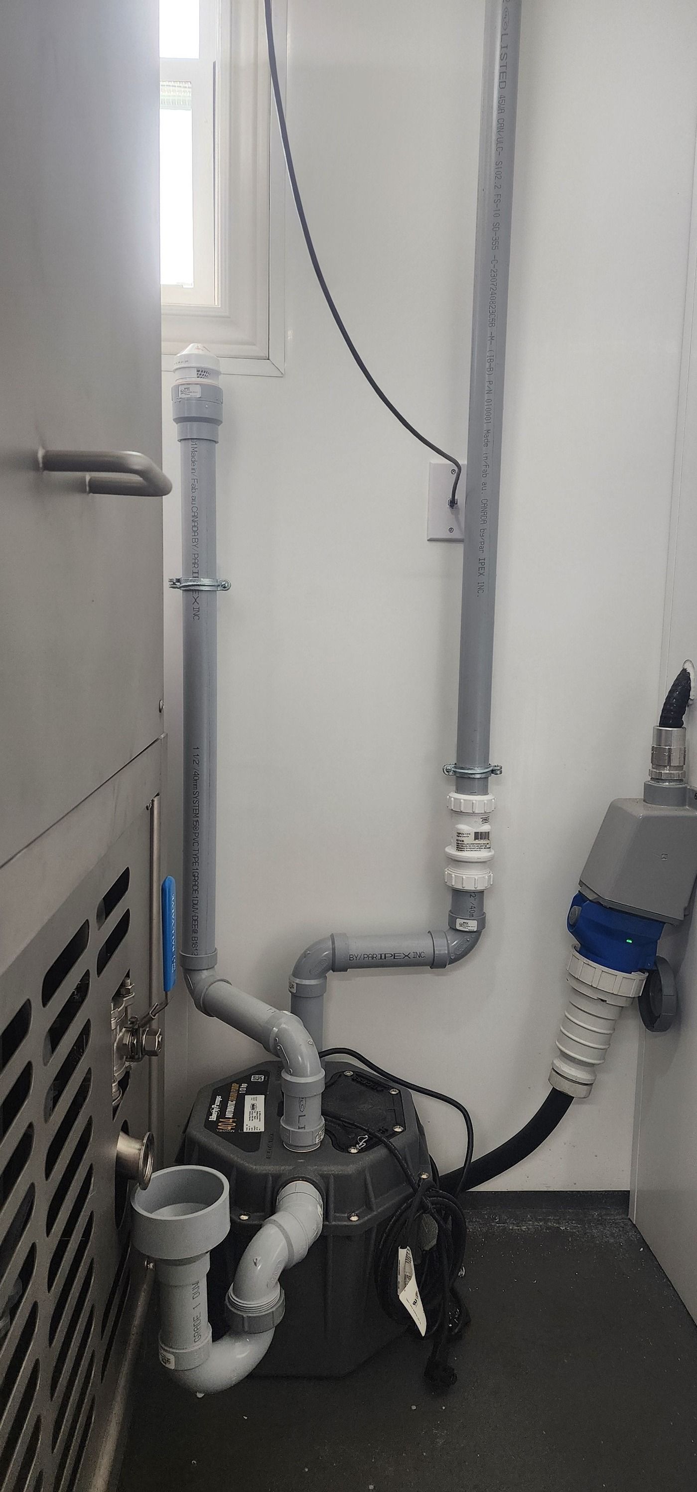 Pipes and a pump against a white wall with a window. Electrical components are visible.