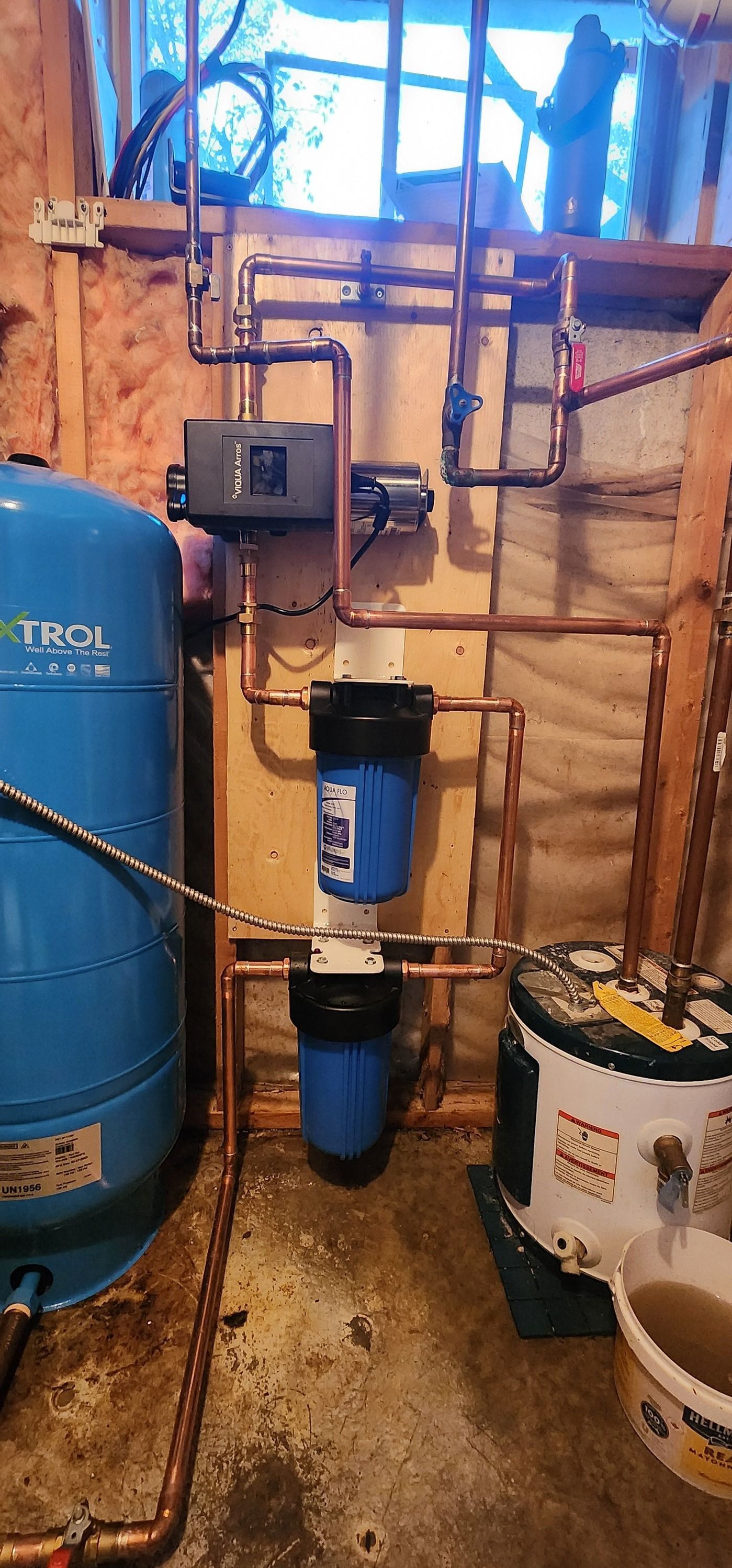 Plumbing system with blue water tank, filters, copper pipes, and a water heater in a basement.