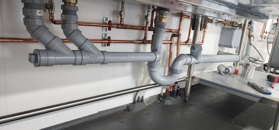 Plumber wearing black gloves uses a red wrench to tighten a pipe under a white sink.