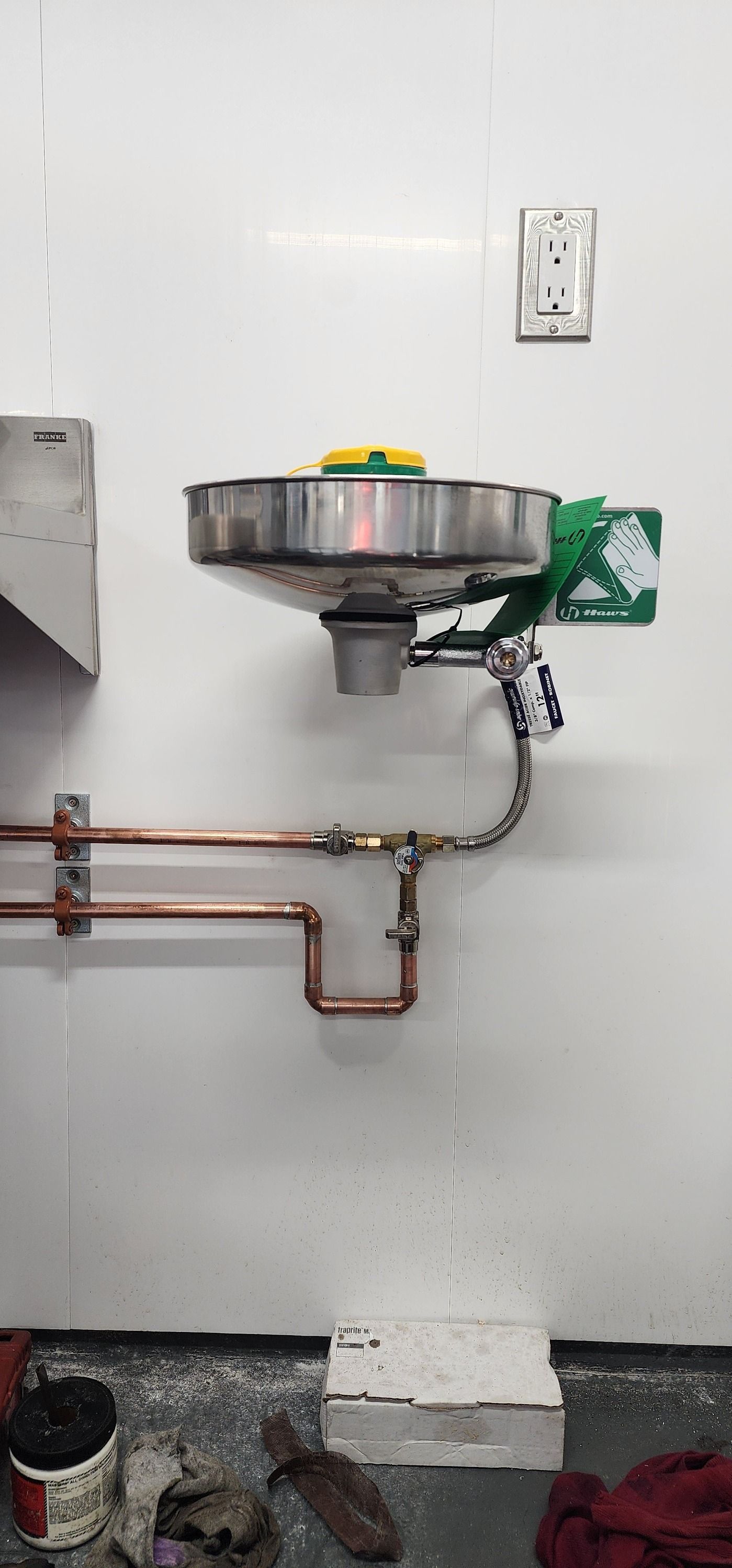 An eye wash station mounted on a white wall with copper pipes.