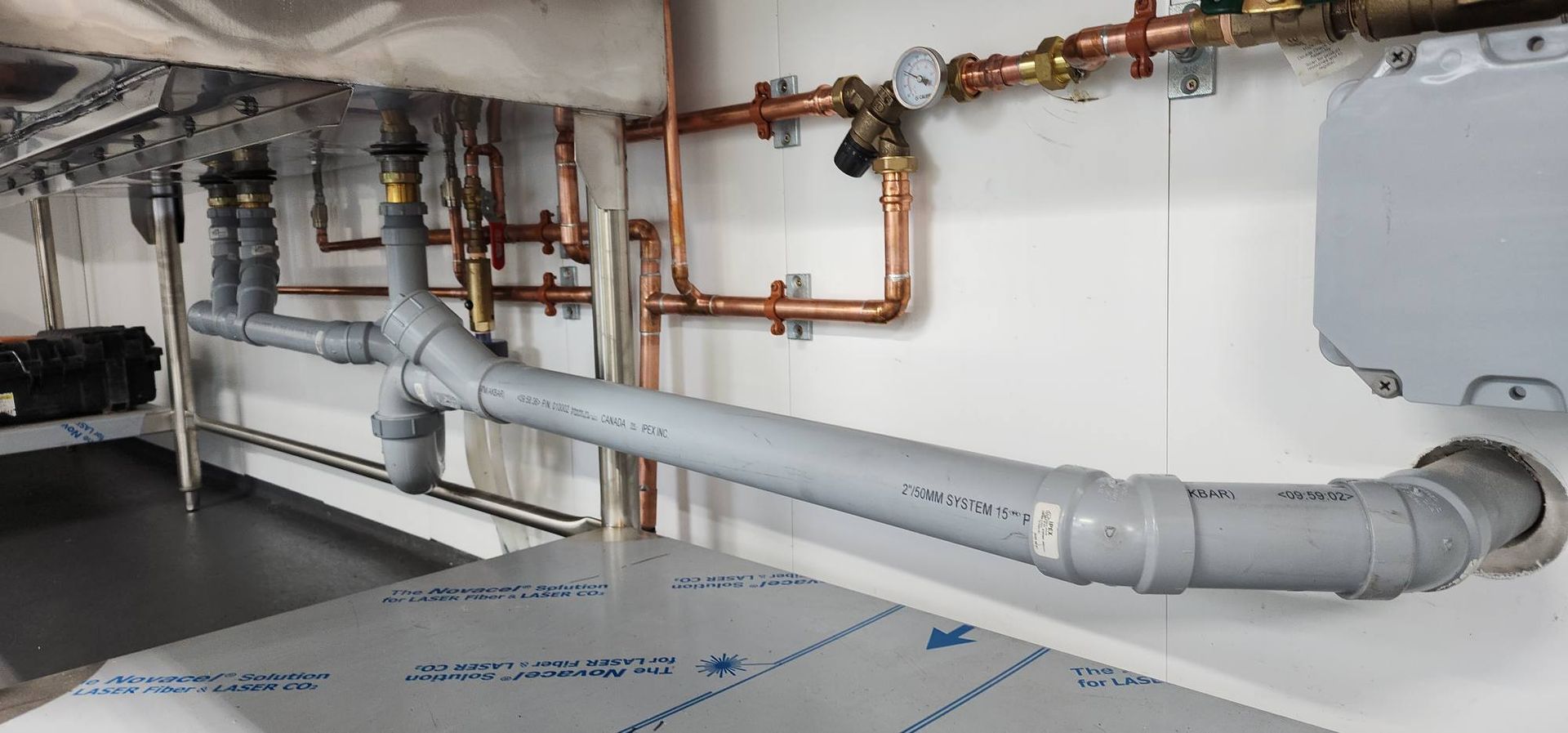 Plumbing system with copper and gray pipes against a white wall.