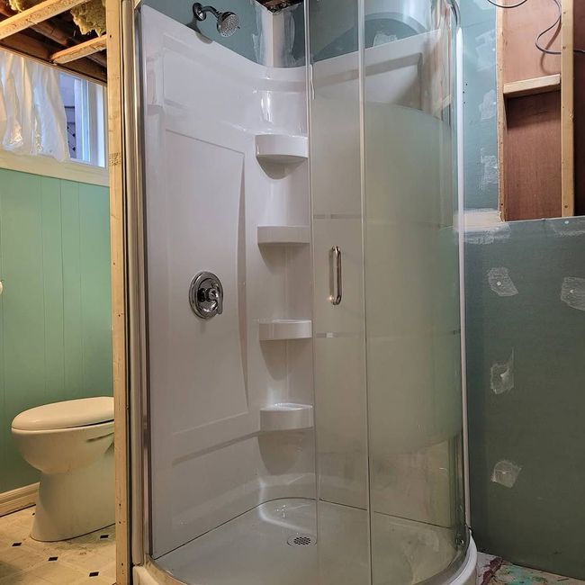 Person in overalls working on plumbing inside a bathroom, tools at the base of the toilet.
