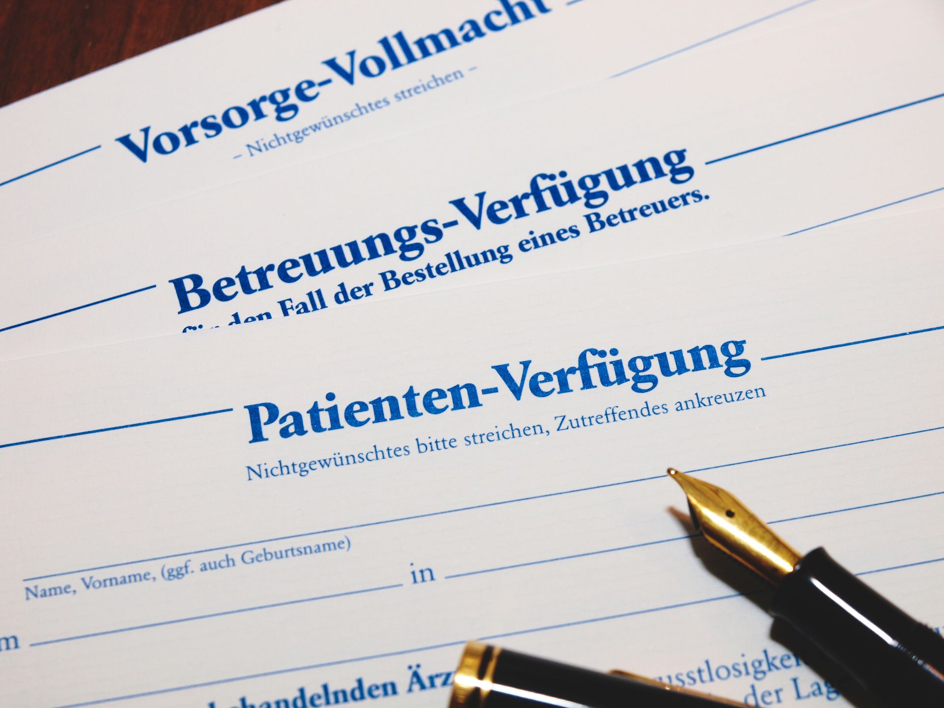 Close-up of legal documents with German titles: Vorsorge, Betreuungs, and Patienten-Verfügung; a pen rests on the paper.