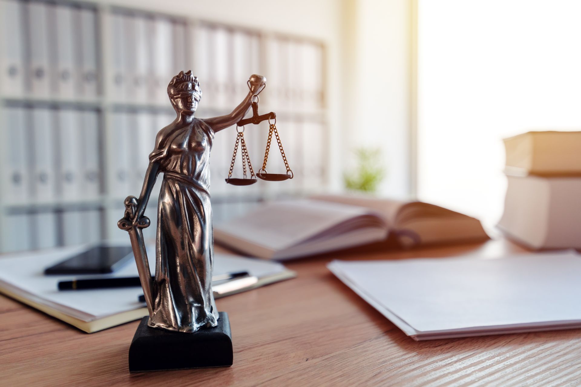Statue der Justitia mit Waage und Schwert auf einem Schreibtisch, Büroumgebung.