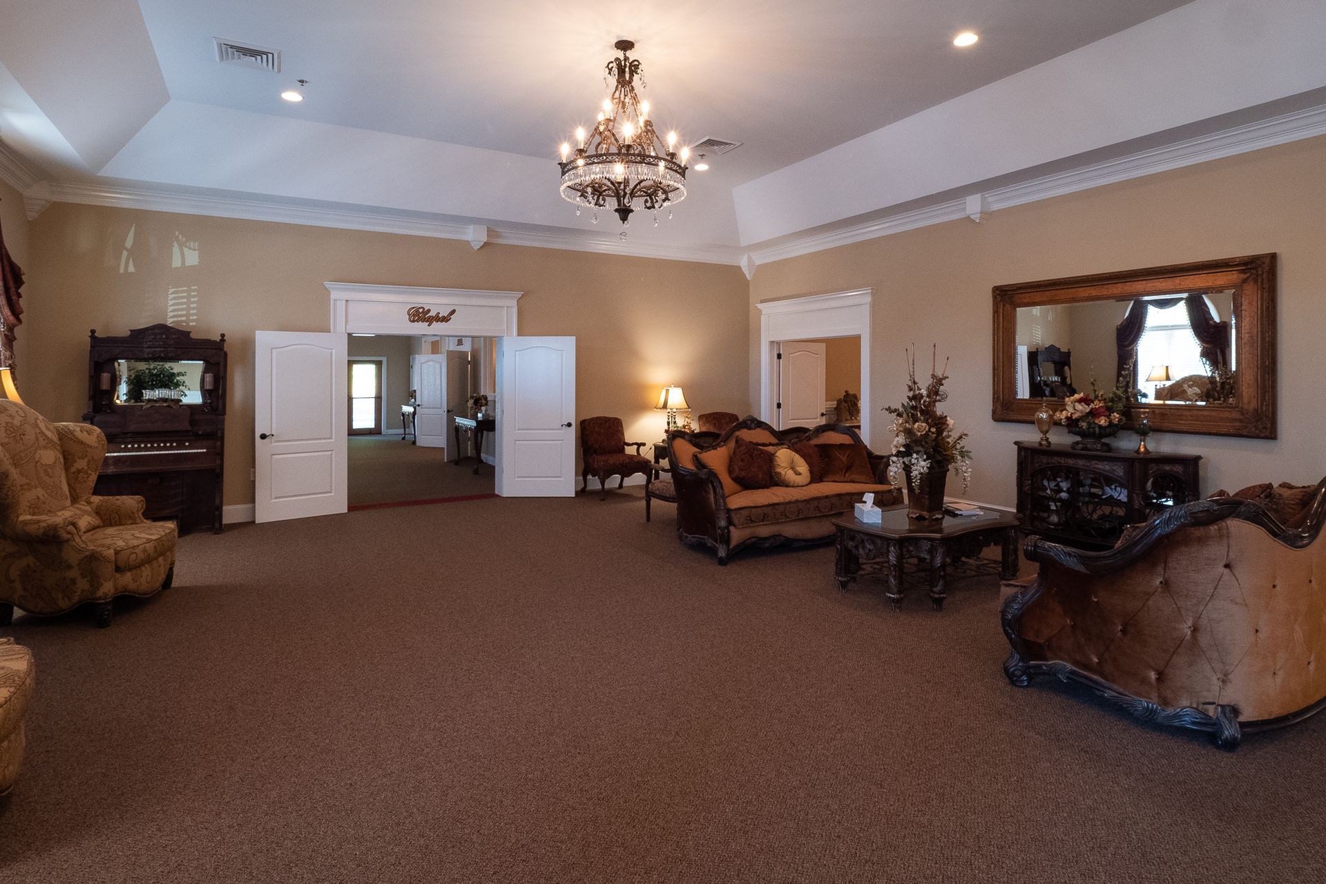 Spacious living room with chandelier, beige carpet, ornate furniture, and mirrors on wood-paneled walls