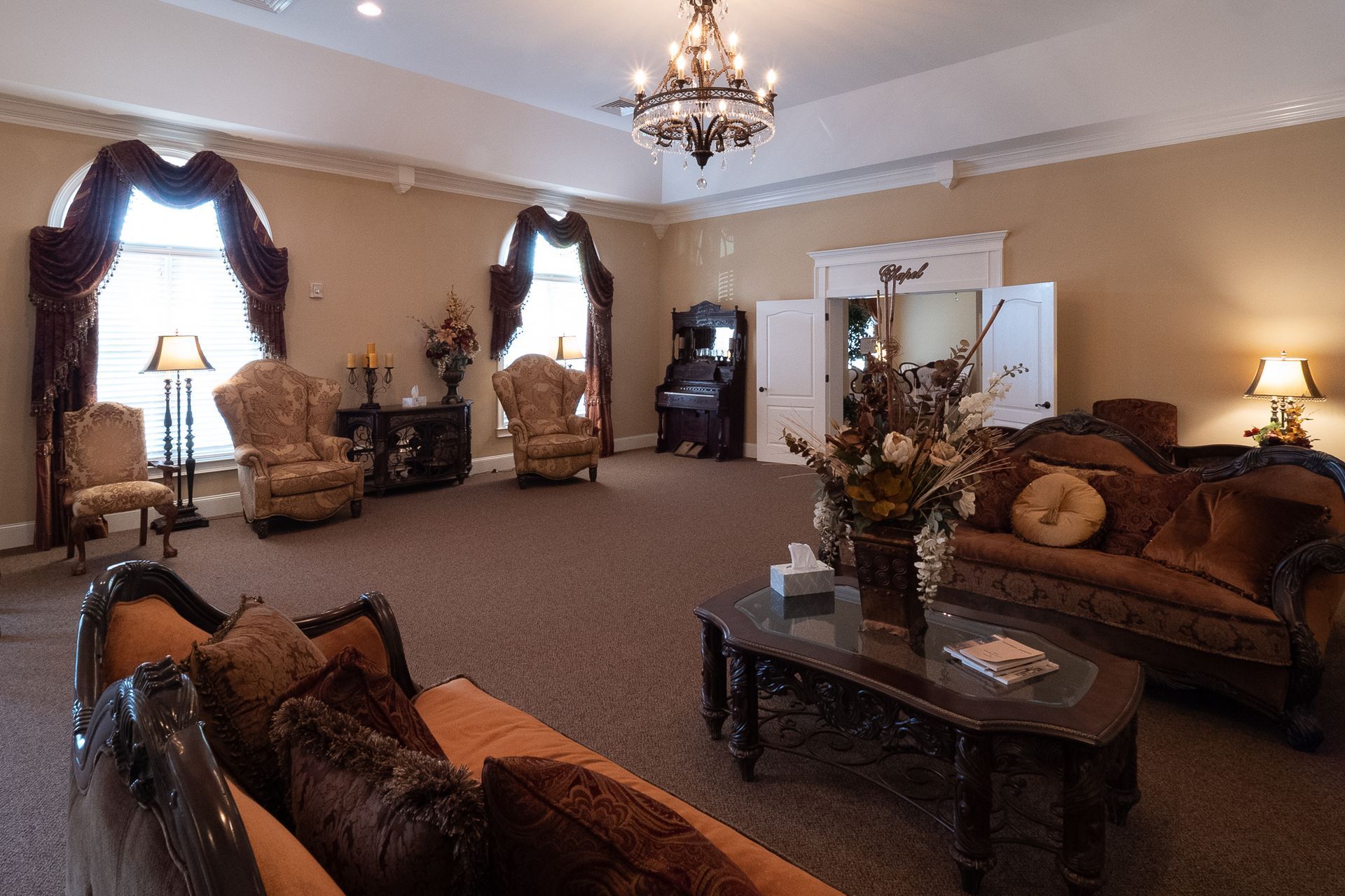 Elegant living room with chandelier, dark wood furniture, and large windows with drapes