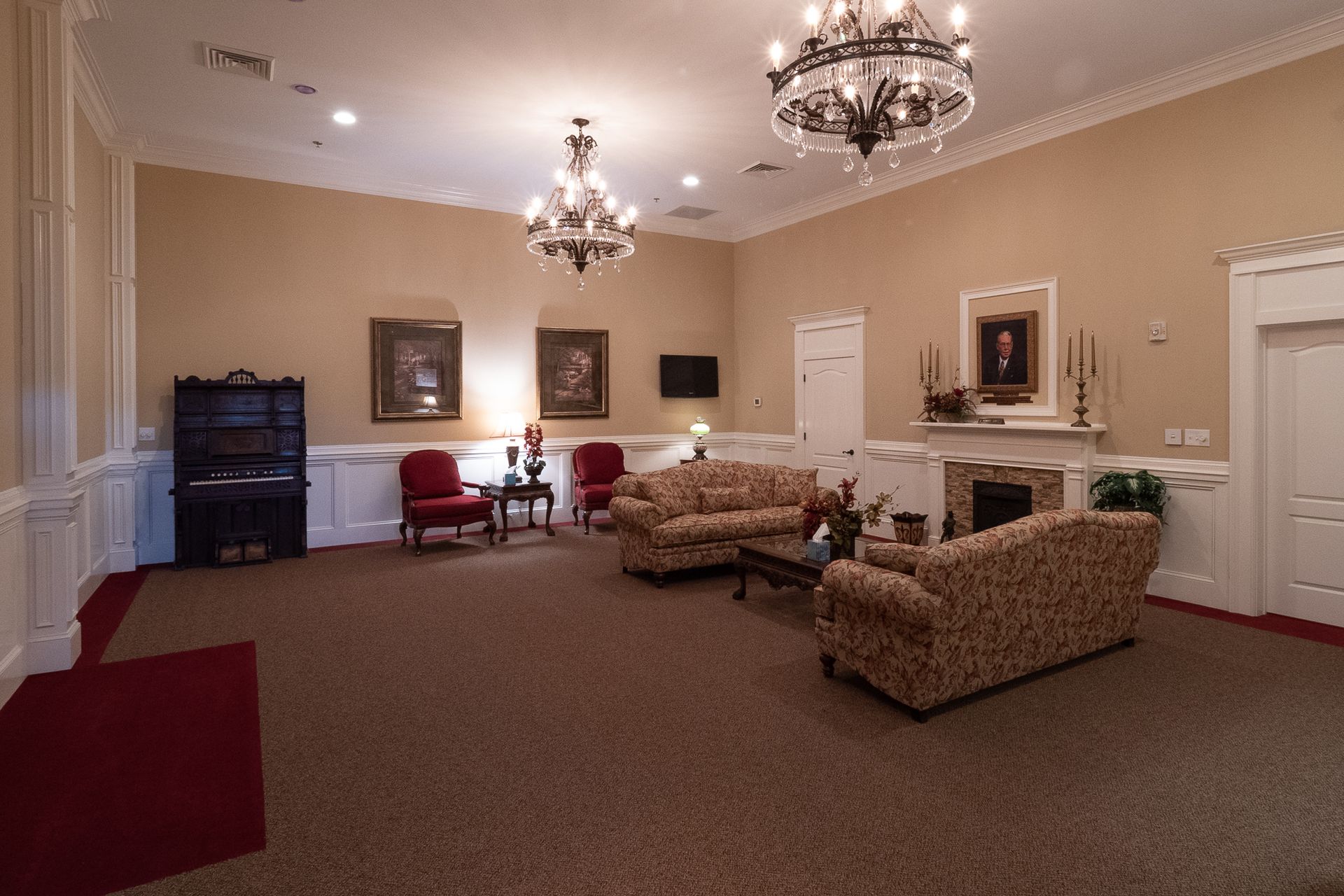 Elegant hotel lobby with red chairs, patterned sofas, chandeliers, and beige walls