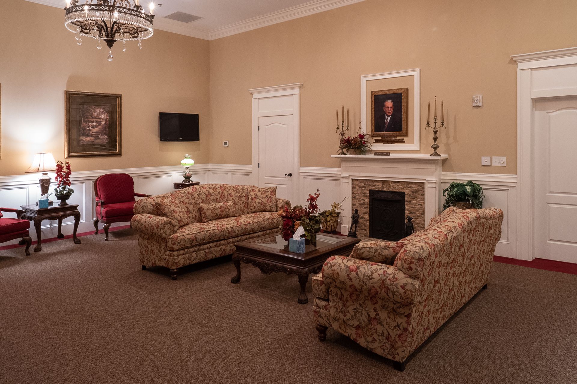 Elegant living room with floral sofas, fireplace, red chairs, and cream walls