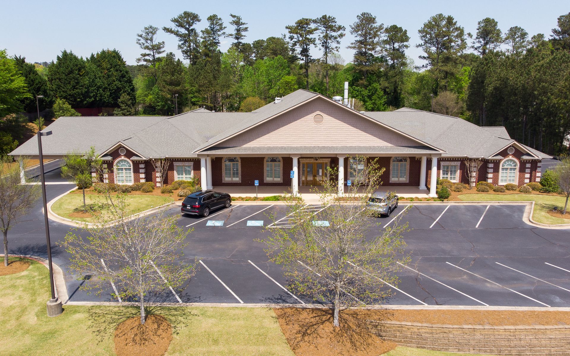 Single-story brick building with a gabled roof and mostly empty parking lot, surrounded by trees