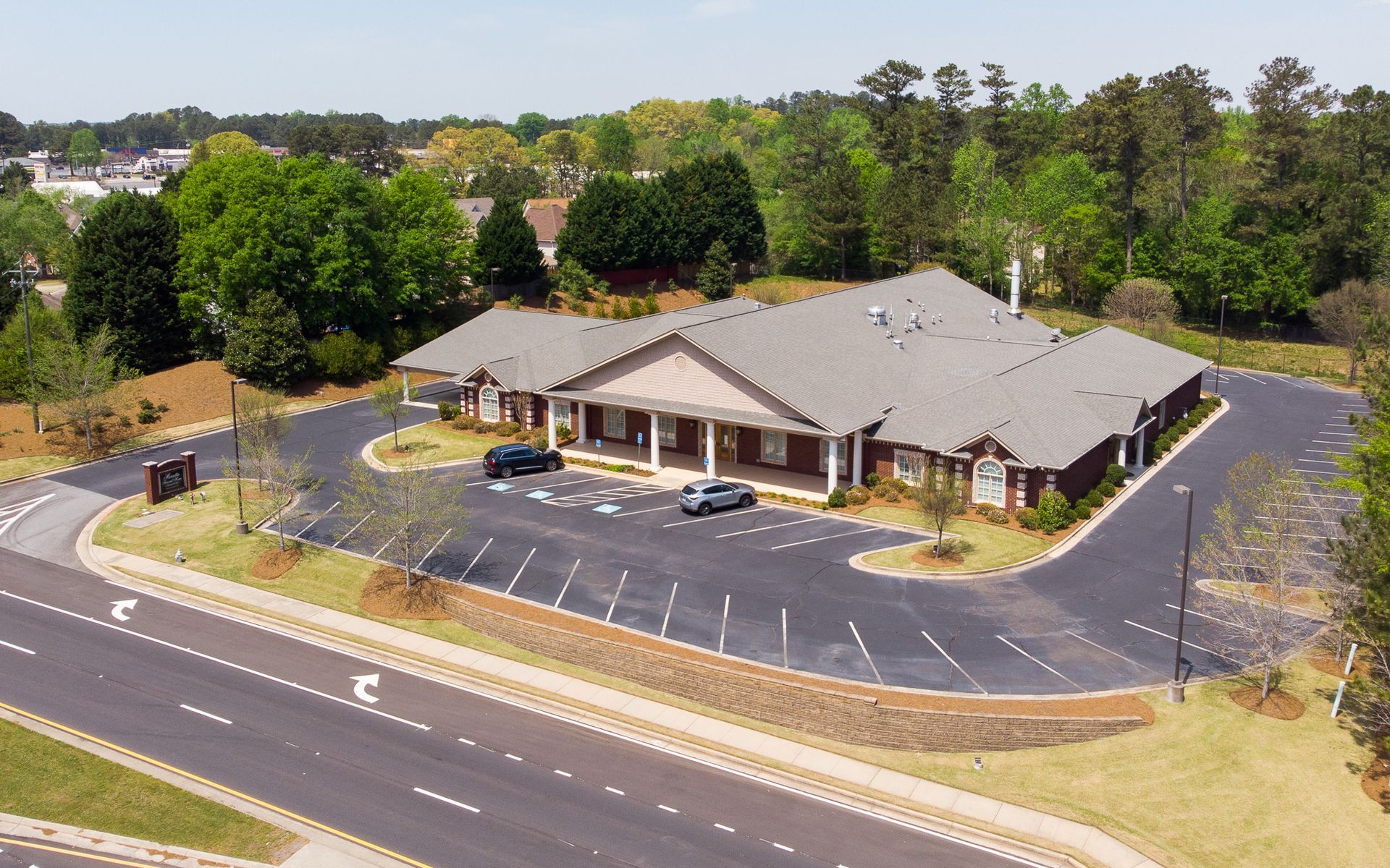 Single-story brick building with parking lot, surrounded by trees and grass on a sunny day