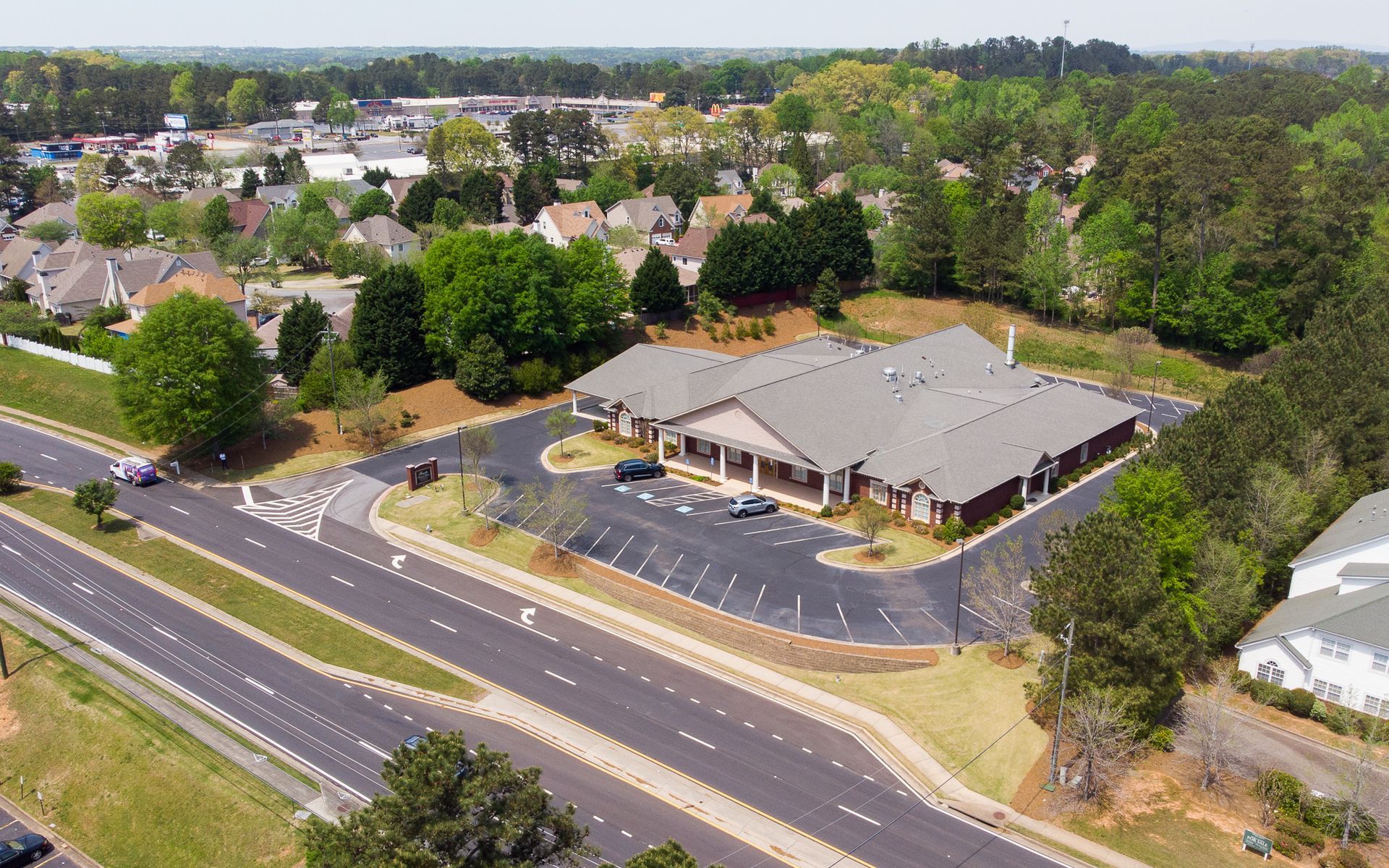 Aerial view of a suburban building with parking lot beside a road and trees.