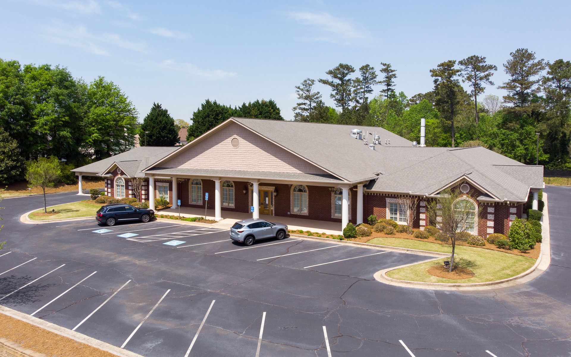 Brick office building with a parking lot and a few parked cars, surrounded by trees