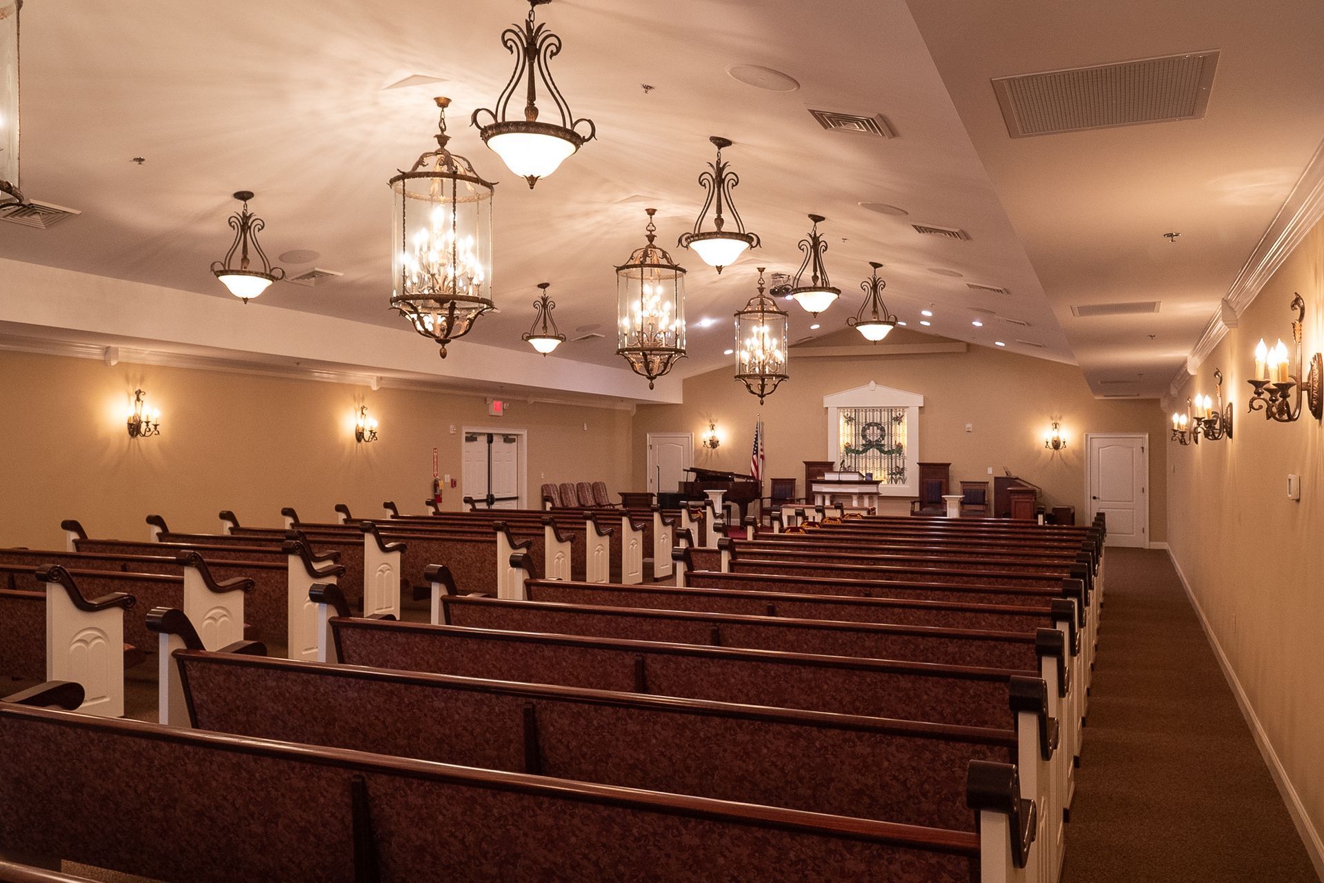Empty church sanctuary with wooden pews, chandeliers, and warm wall lighting