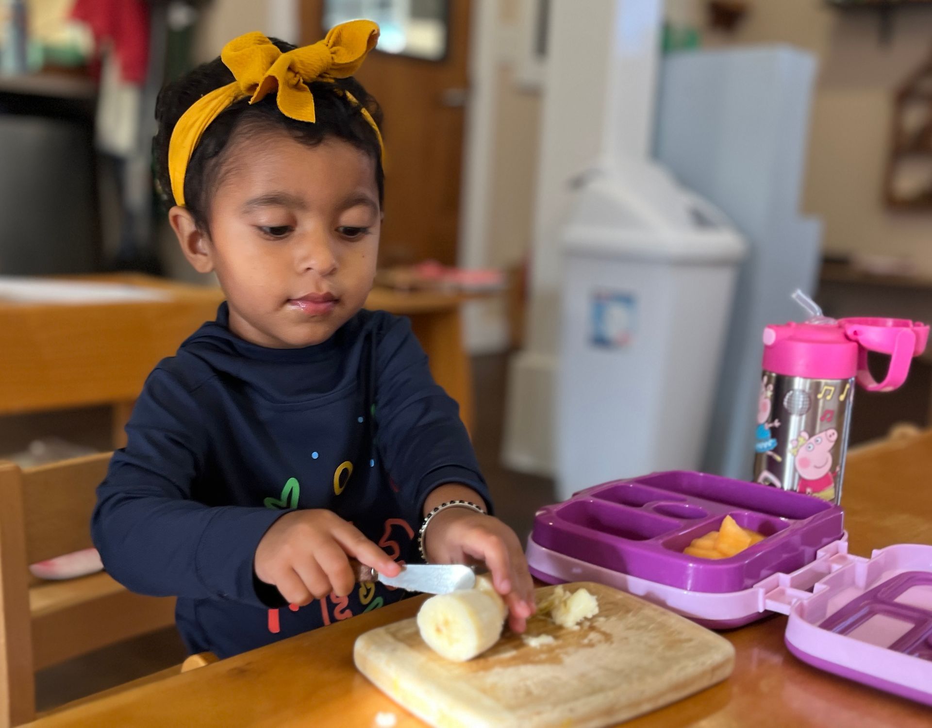 A Montessori little girl is cutting a banana on a cutting board