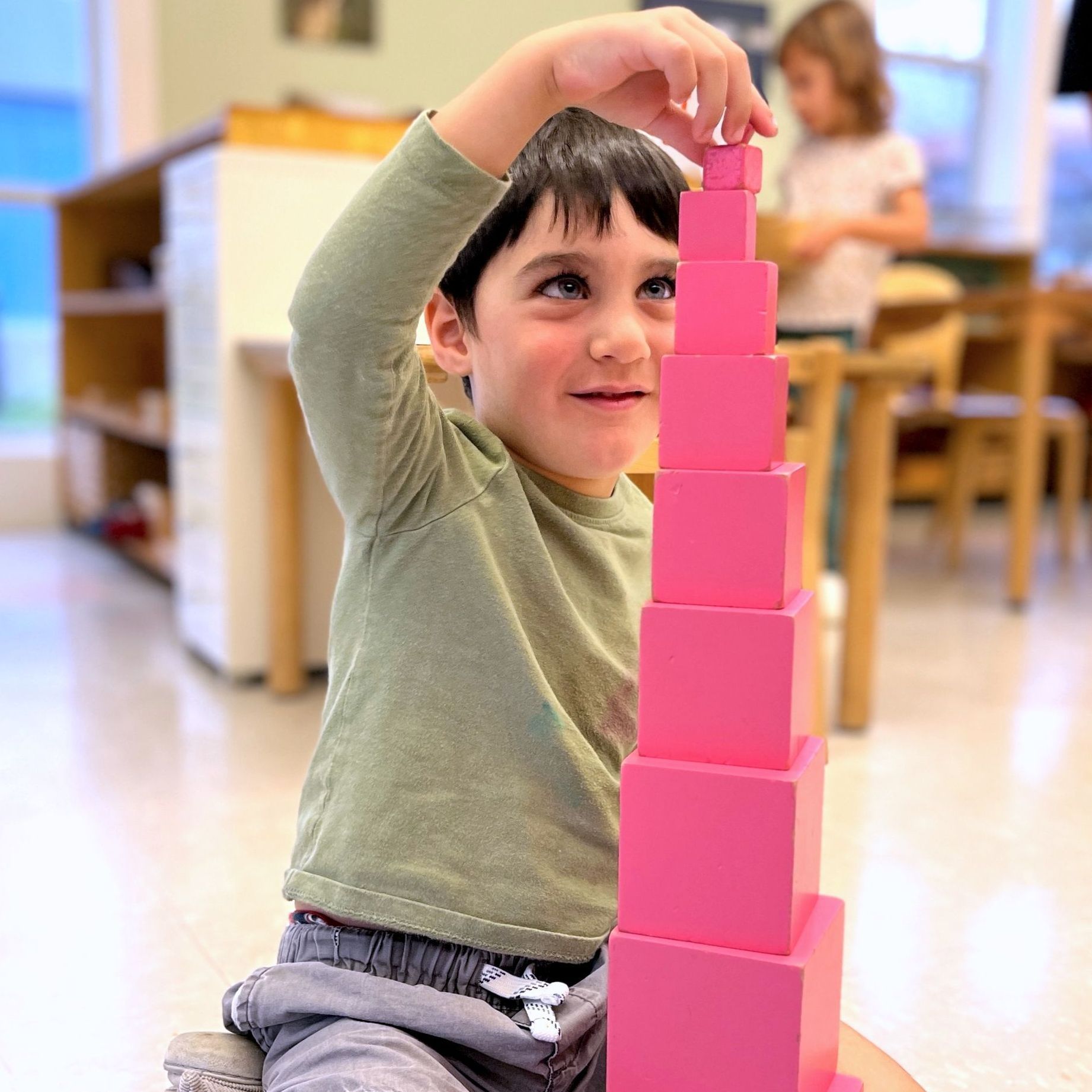 A Montessori young boy is stacking pink blocks on top of each other
