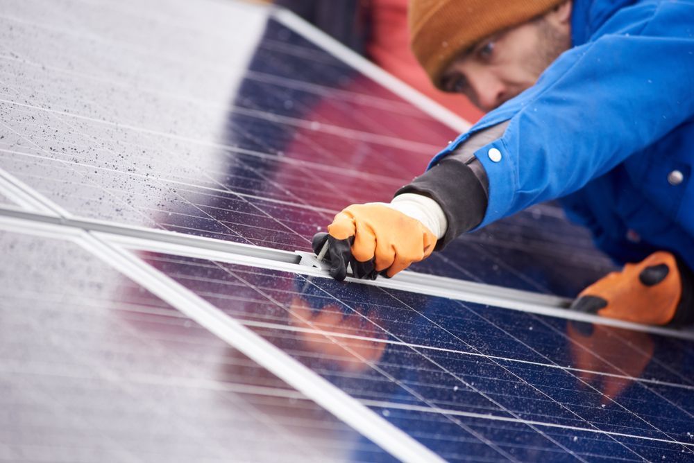 Man in Jacket and Orange Gloves Installing Solar Panels Outdoors — Big Electrics in Redlynch, QLD