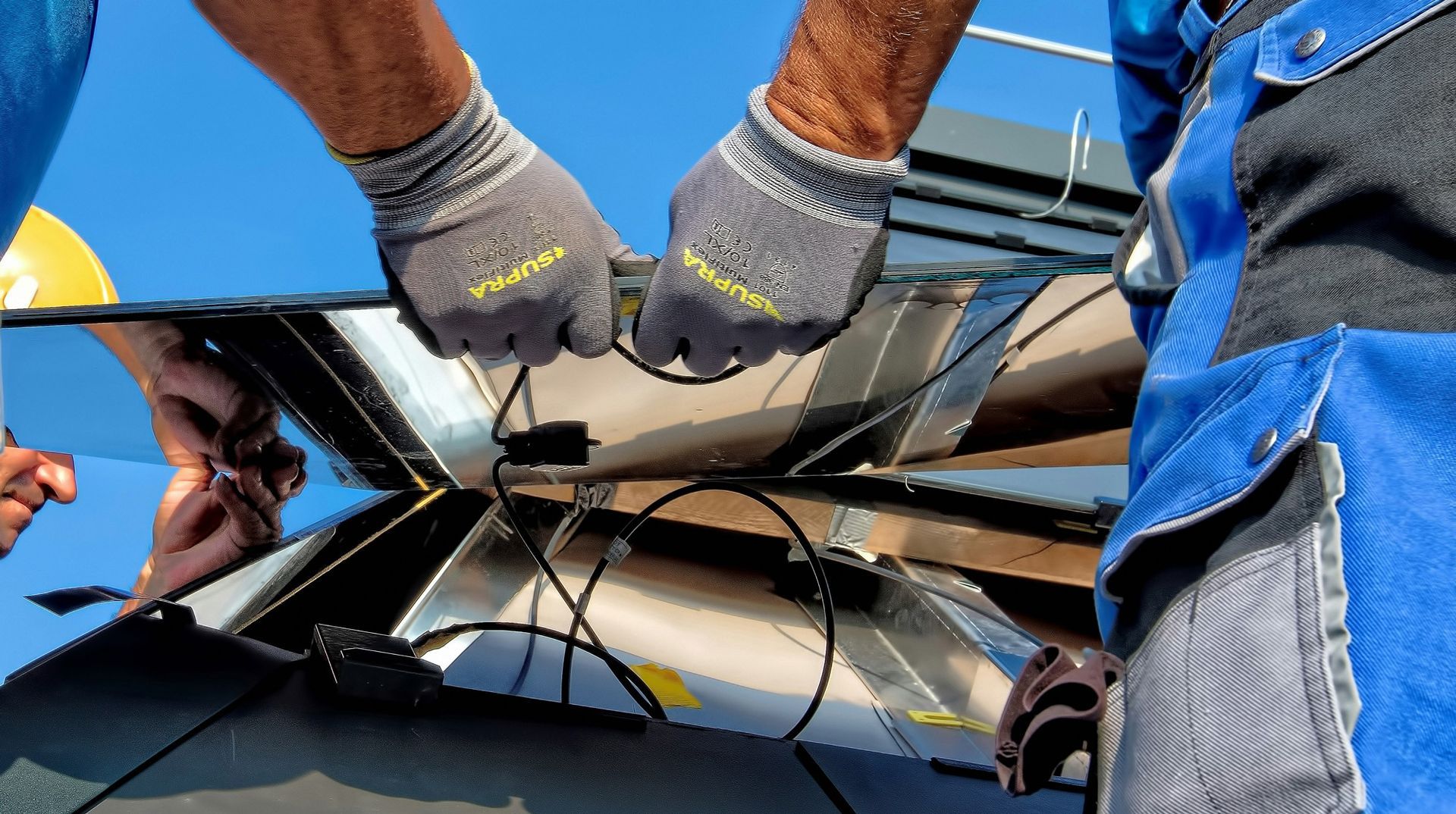 Two Workers Connecting Wires to a Set of Solar Panels — Big Electrics in Redlynch, QLD